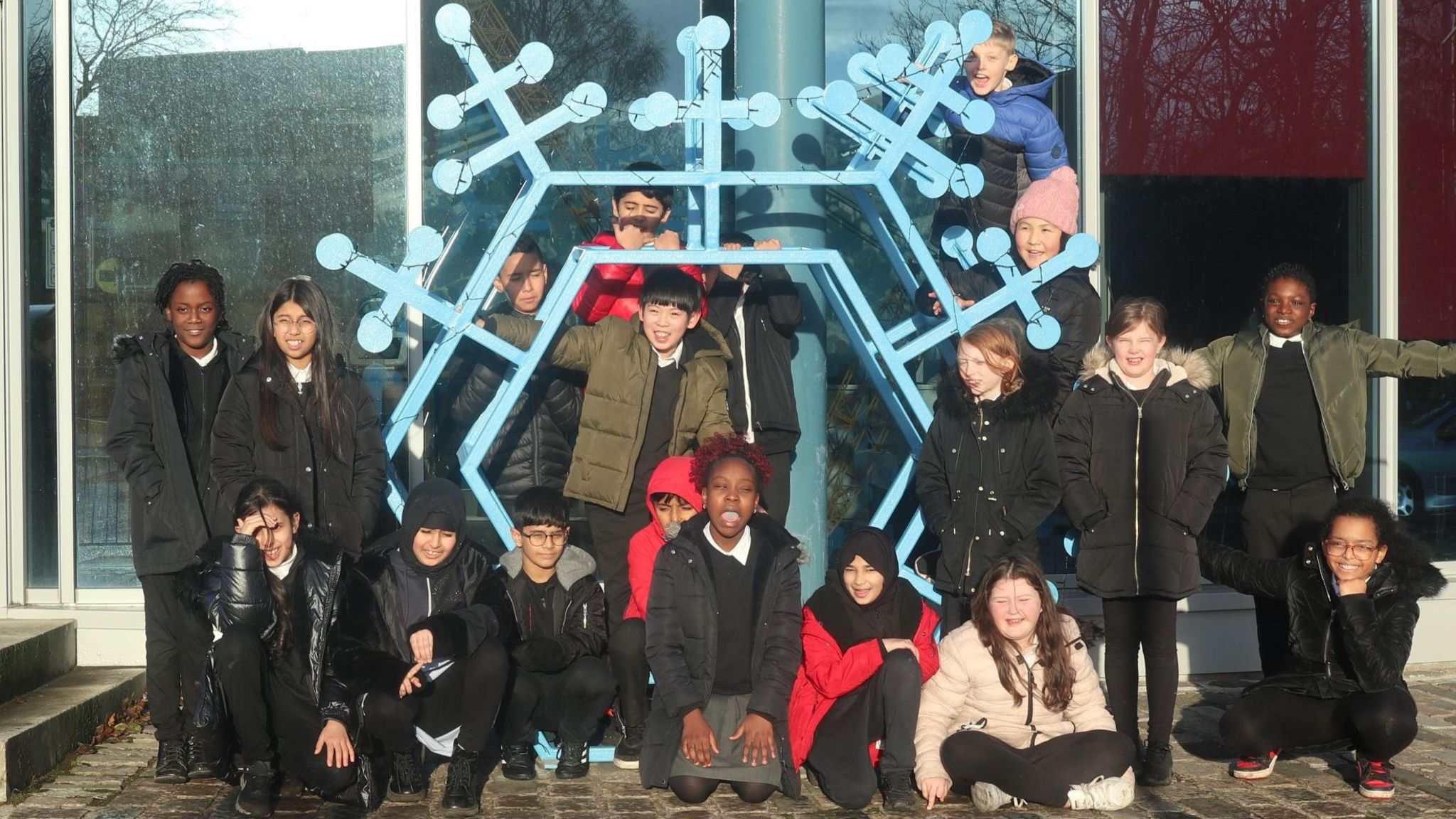 Group of school kids standing in front of a metal snowflake
