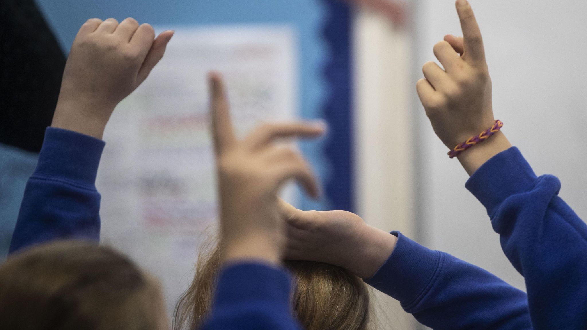 Anonymous schoolchildren wearing blue putting their hands up in a class