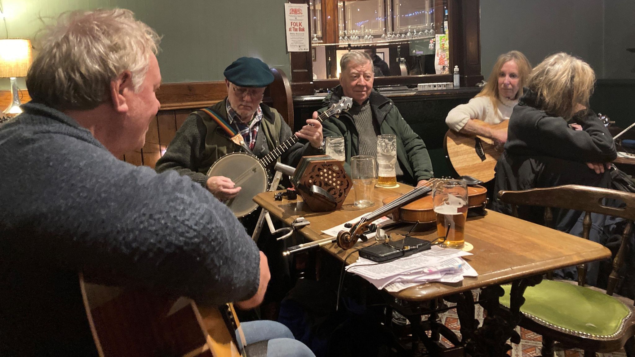 Five people in a pub room with guitars and other instruments