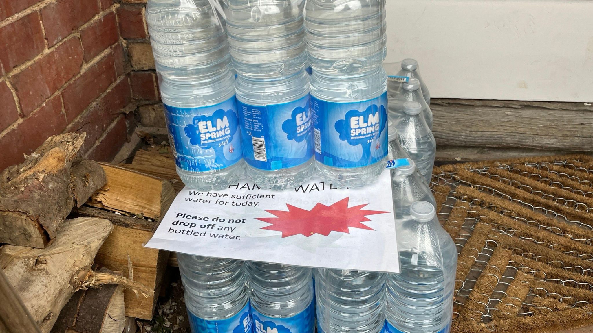 Bottled water sits outside a house along with a sign saying "please do not drop off any more bottled water"