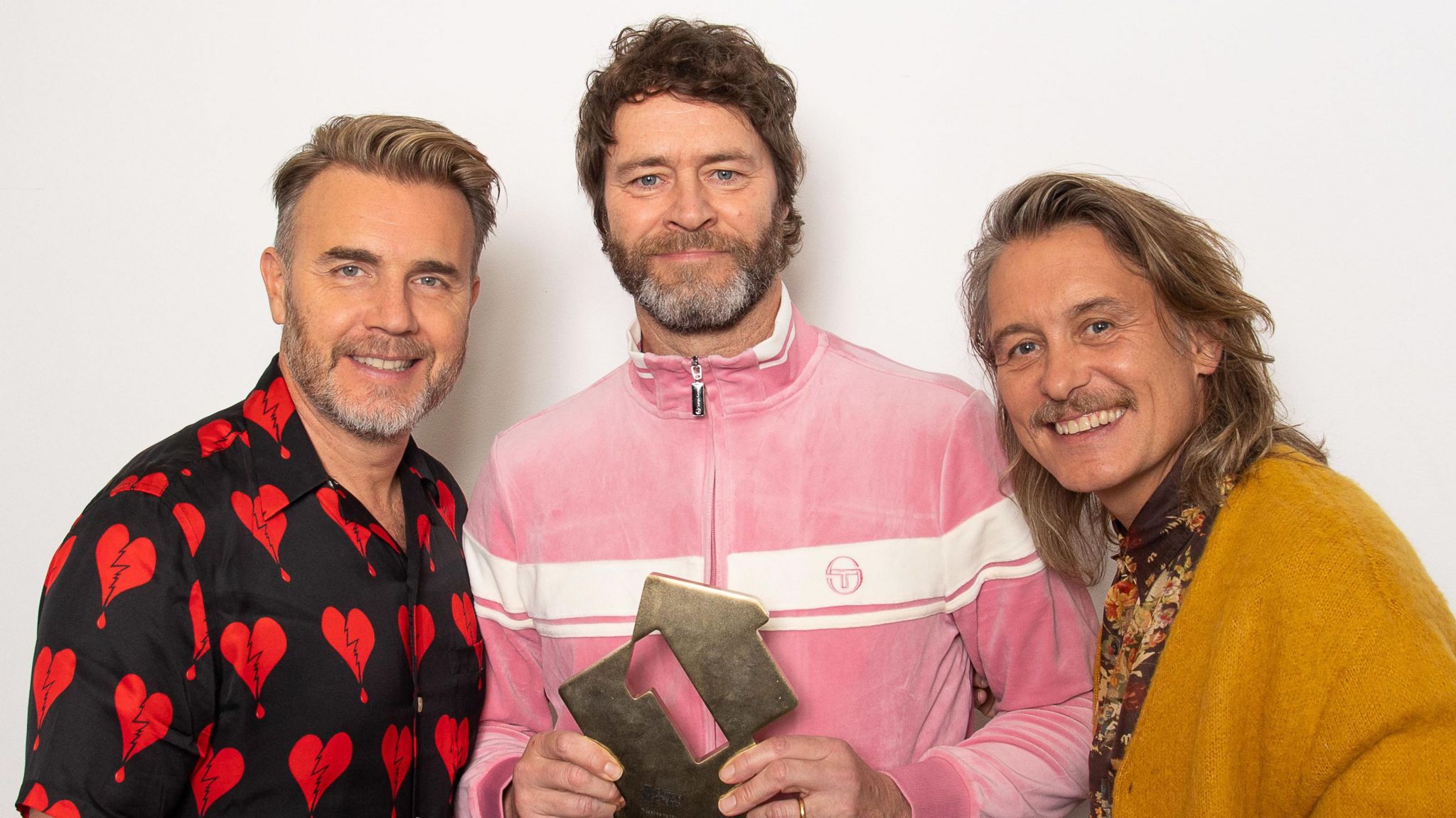 Gary Barlow, Howard Donald and Mark Owen, with Howard Donald holding a Number 1 award for their number one album This Life in December 2023