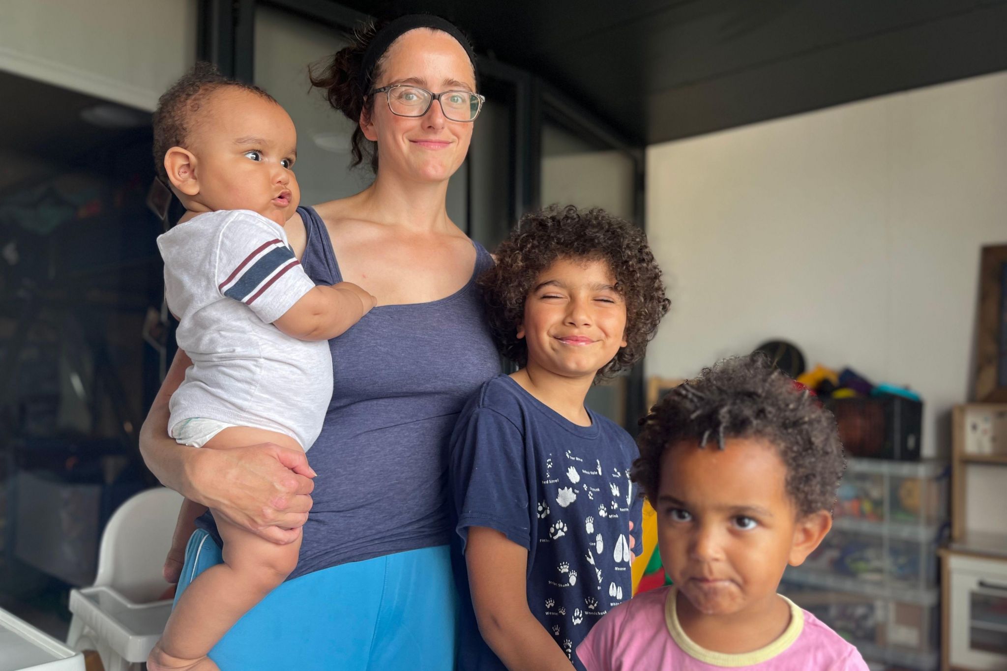 A woman with curly brown hair and glasses, Thea, with her three children: Isaac, a baby, JJ, aged two, and Moses, 9