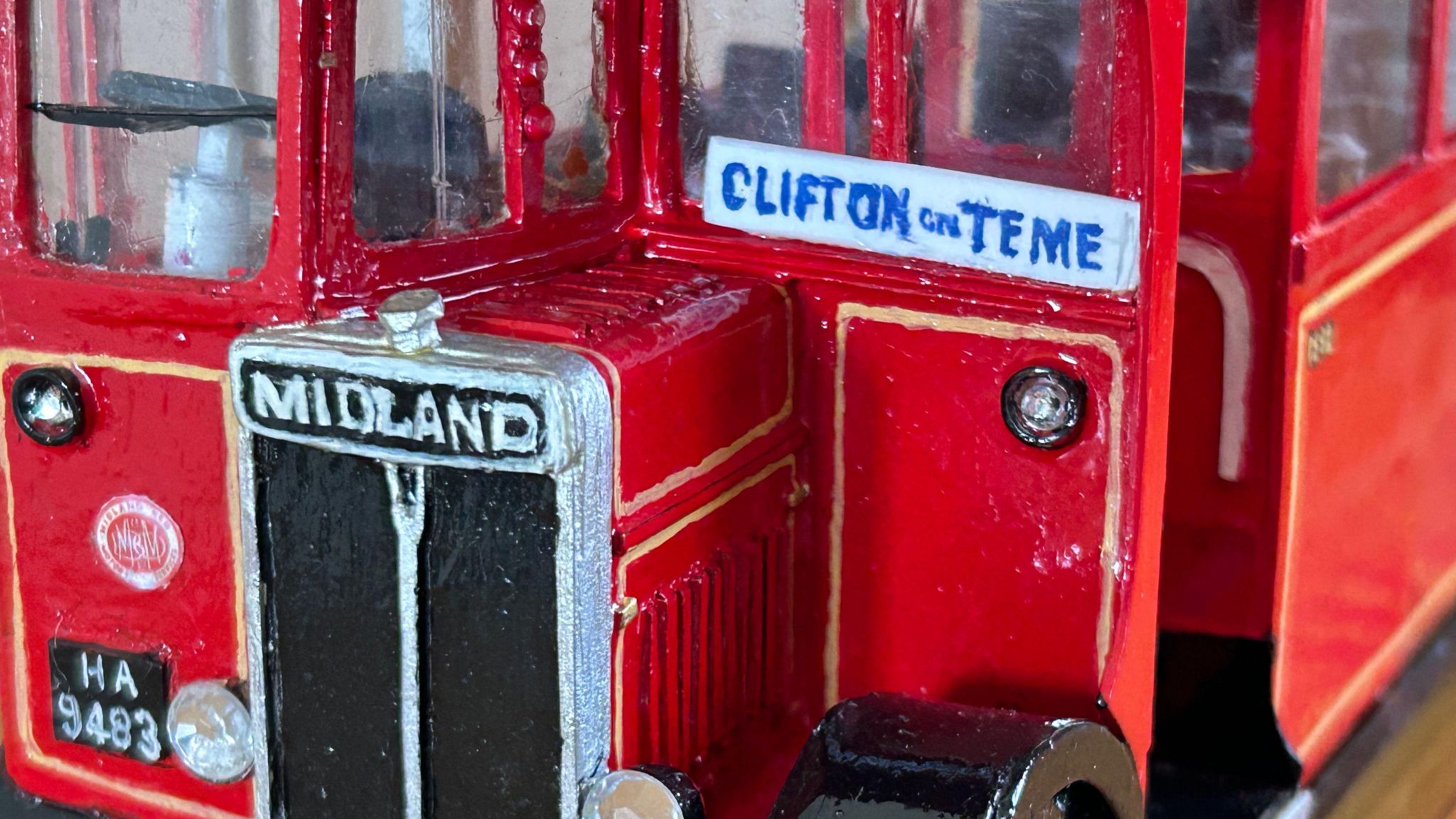 A close-up image of a replica bus. It is red, and says "Clifton on Teme"