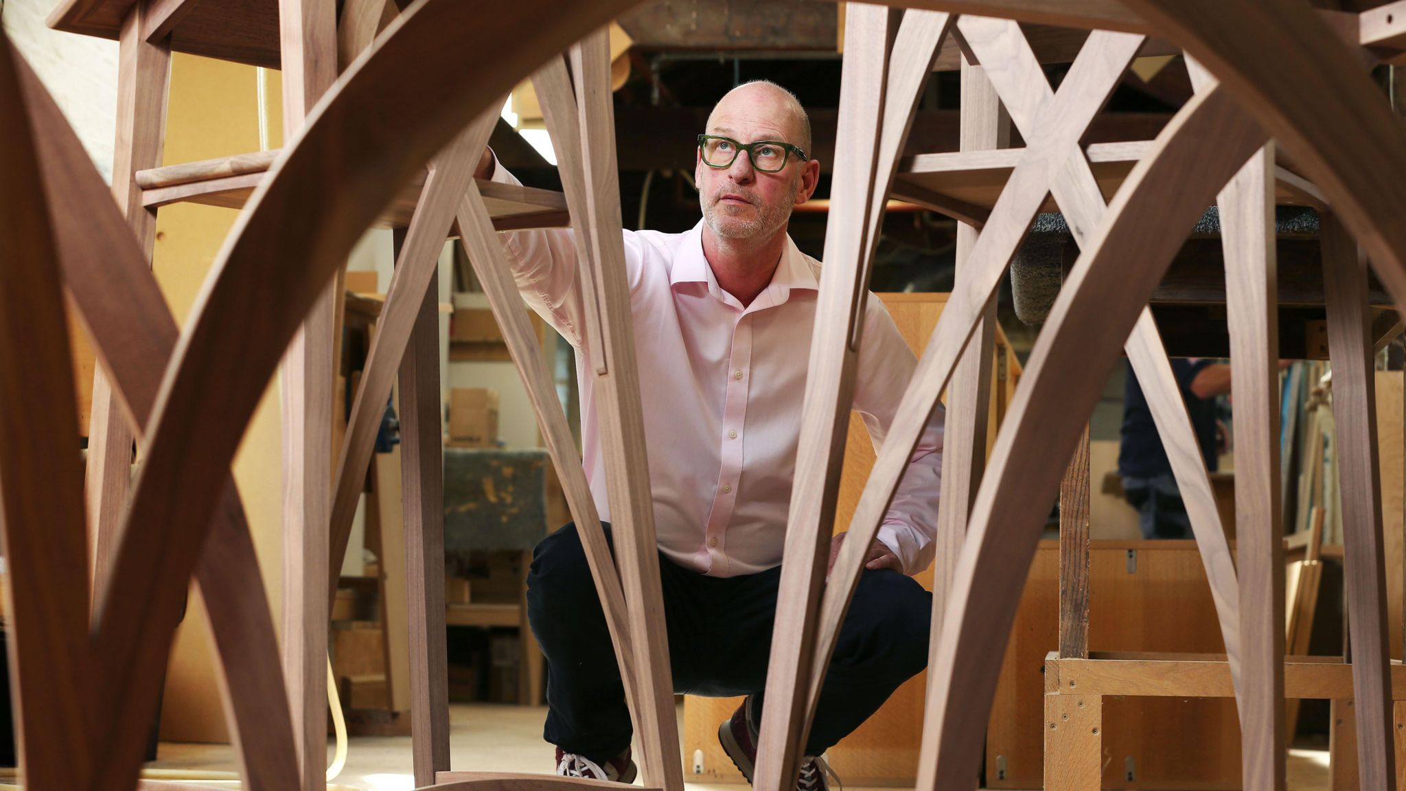 A man is pictured kneeling down among some traditionally built wooden stools