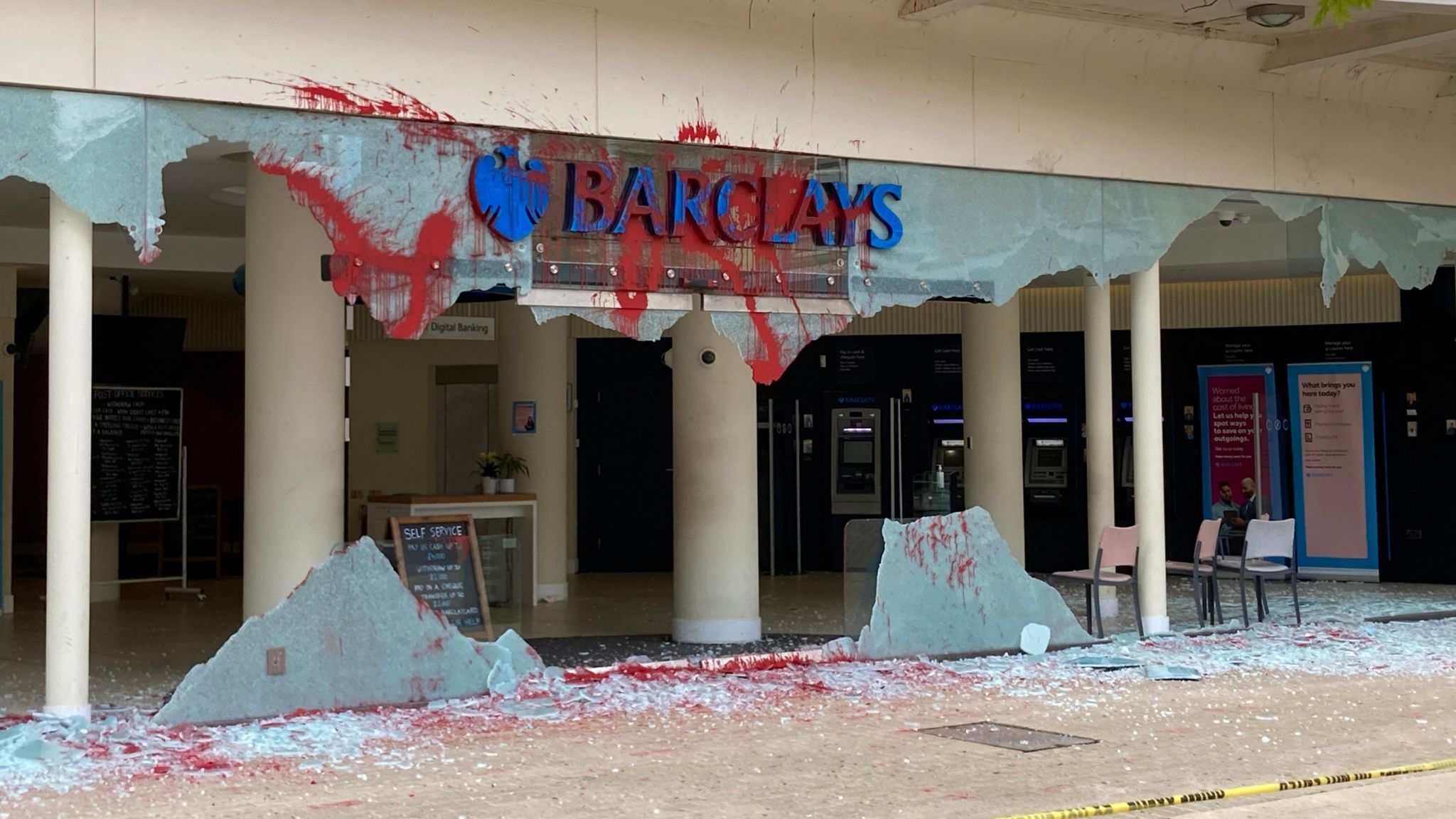 Smashed window at the entrance of Barclays Bank with red paint sprayed around building 