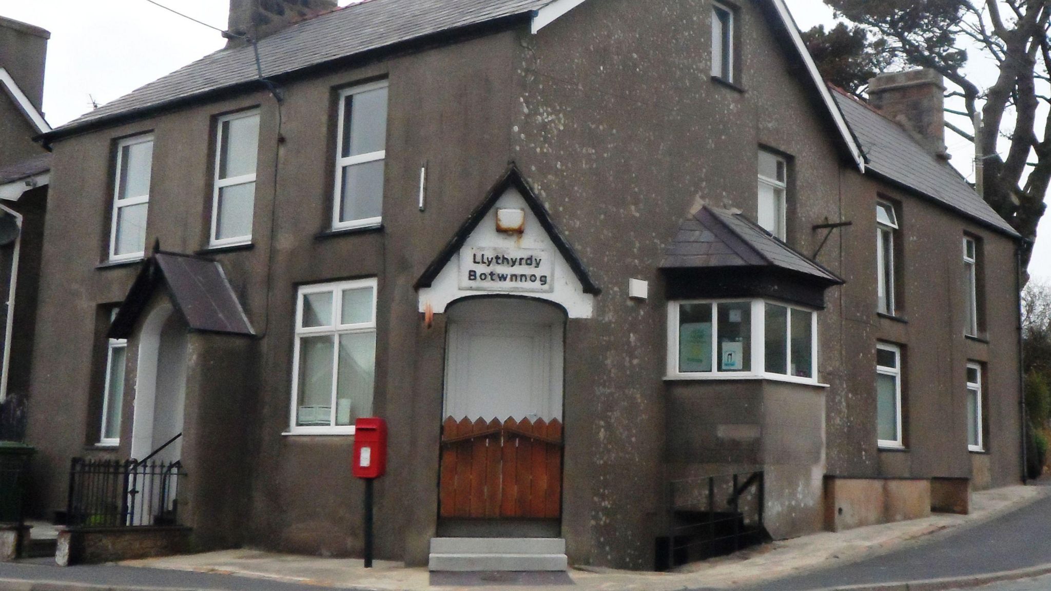 A grey post office building with a red post box outside in the village of Botwnnog