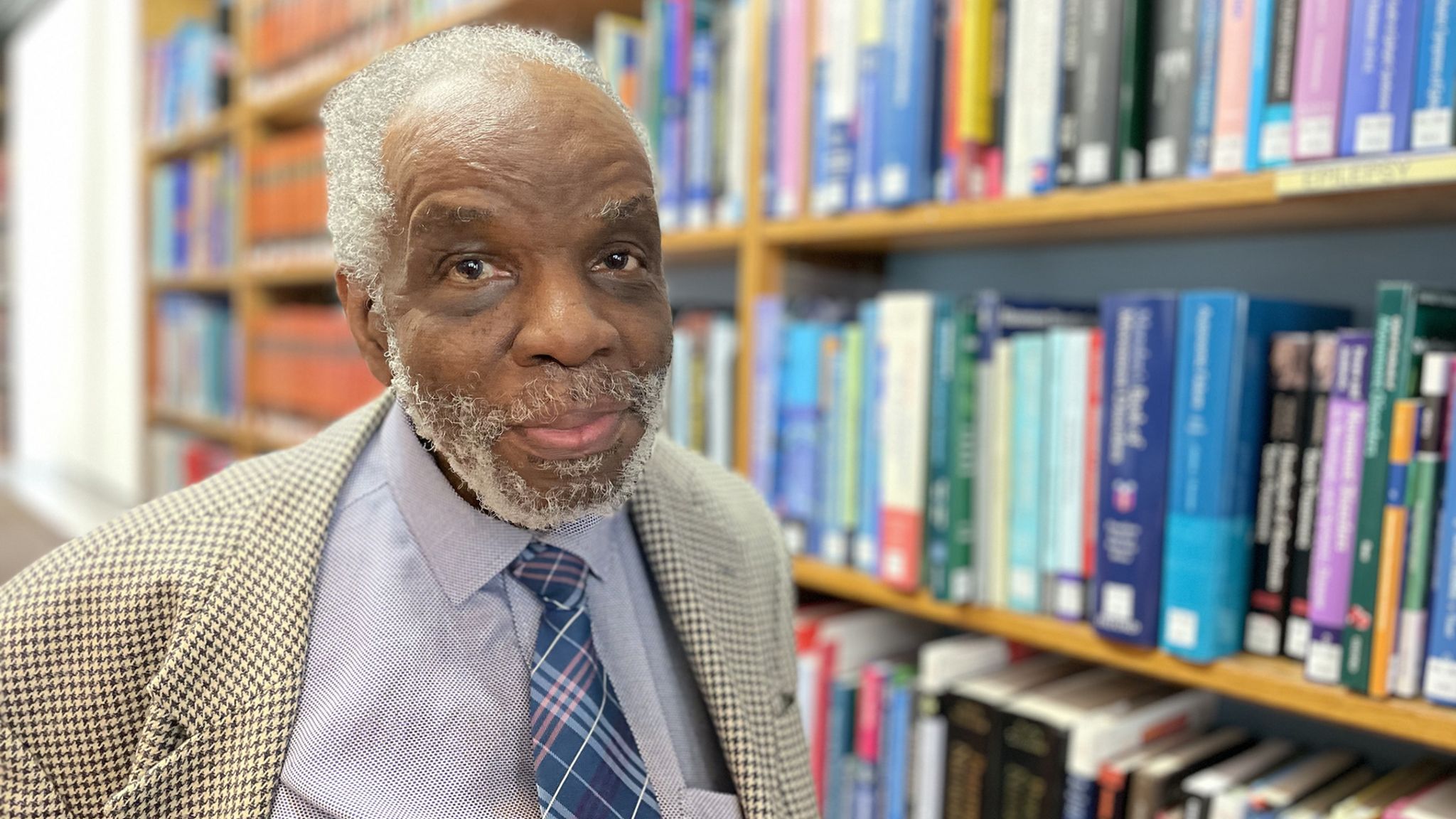Portrait of Dr Aggrey Burke in front of shelves of books