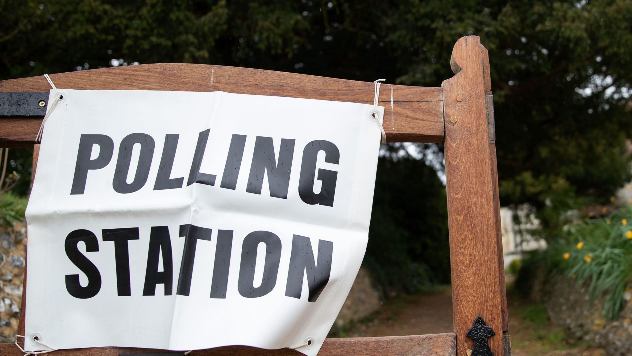 A white polling station sign tied to a wooden gate at the end of a narrow path.