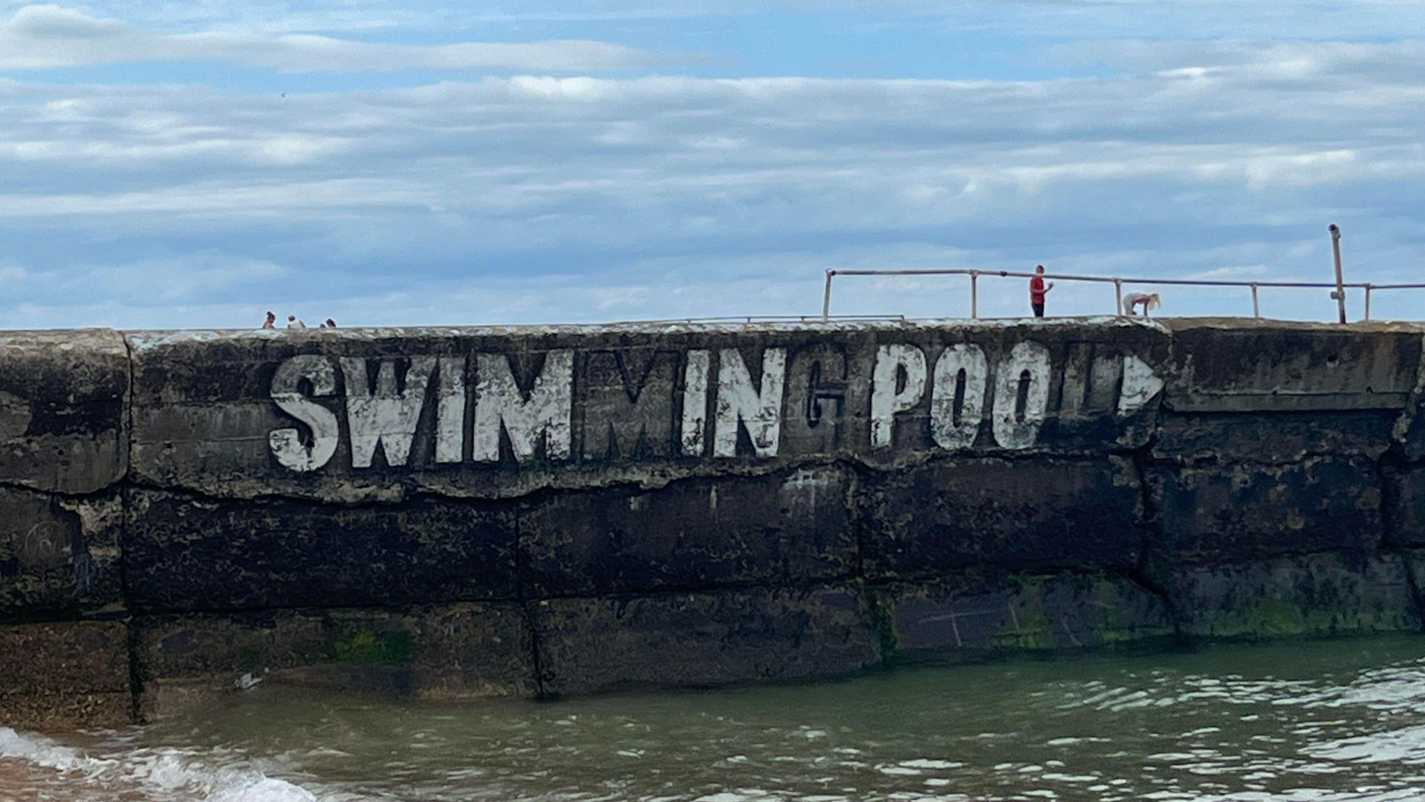 A large sign saying swimming pool in white has had certain letters painted out to read 'swim in poo'.