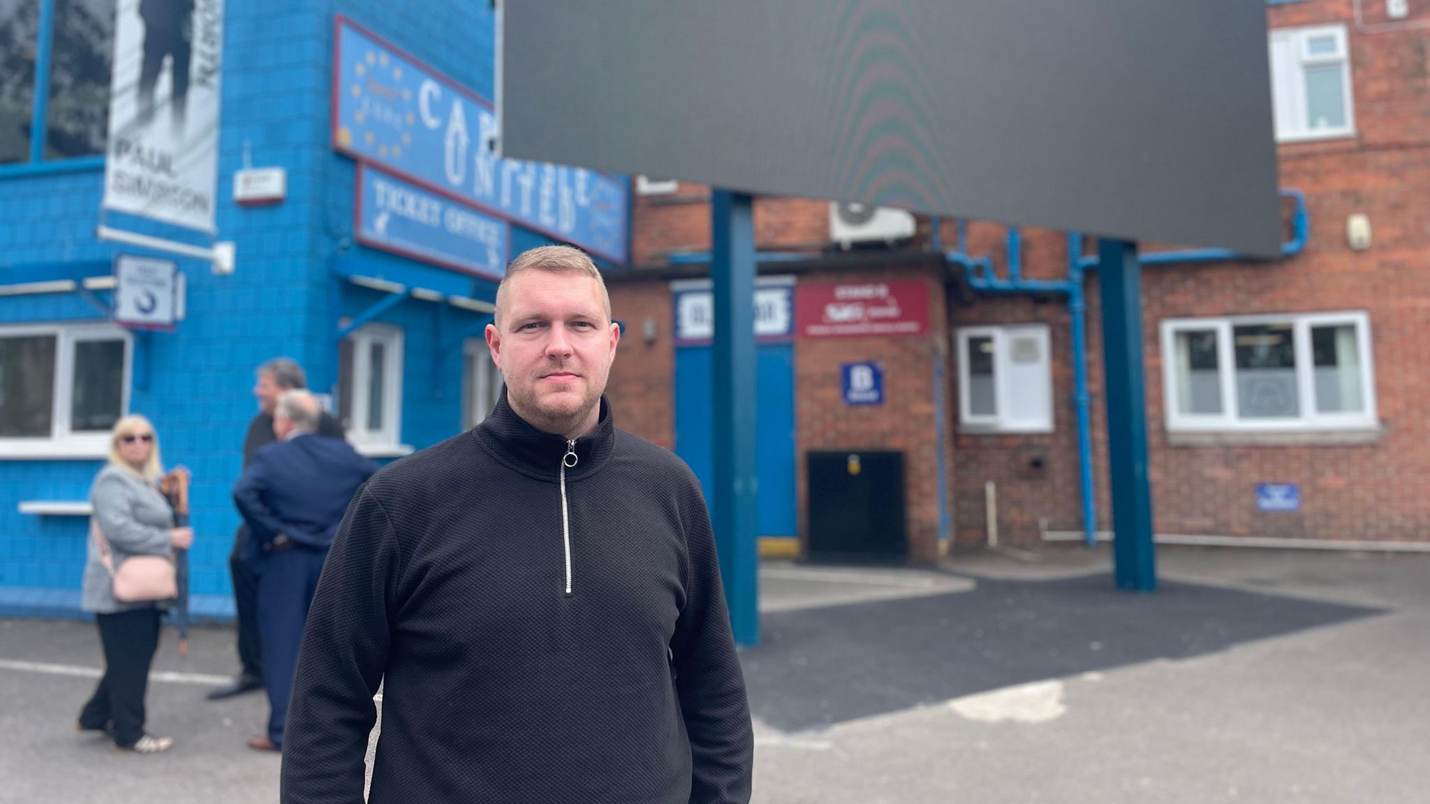 A man in a hoodie standing outside Carlisle United 