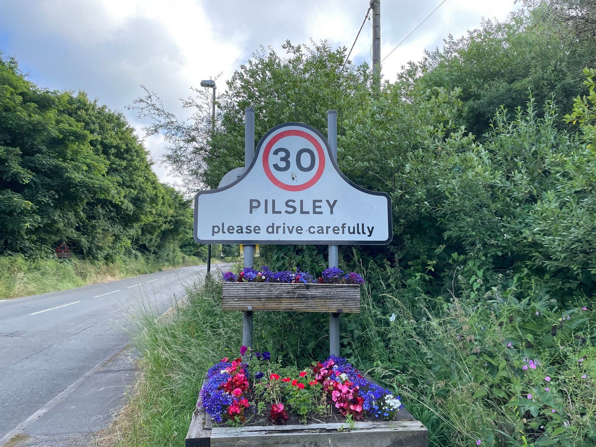 Pilsley road sign and flowers in planters