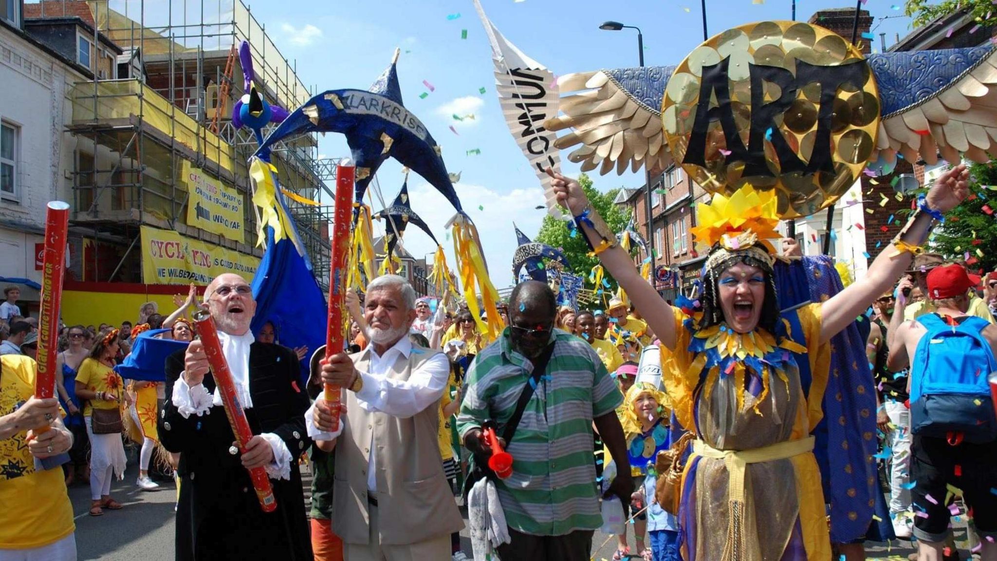 Carnival goers dressed in yellow and blue with sequins and sparkles on their costumes, throwing confetti into the air