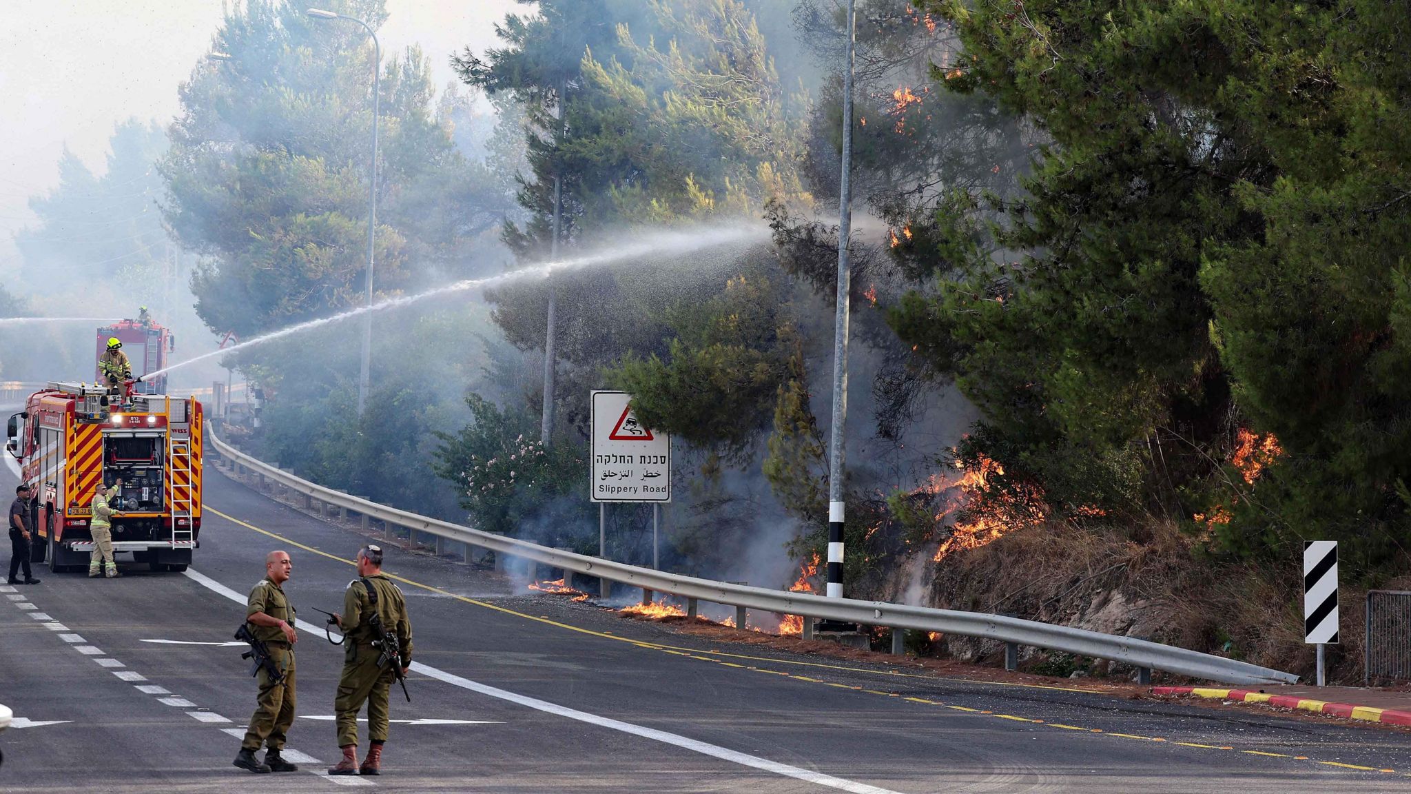 Soldiers stand near a fire engine spraying water on a forest fire