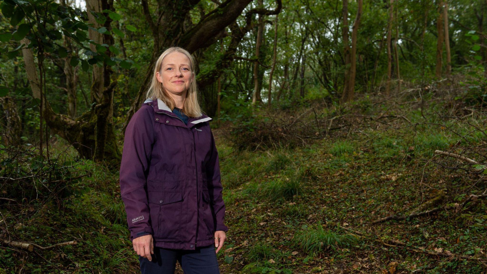 Rachael Fickweiler stood in a woodland, wearing a purple coat