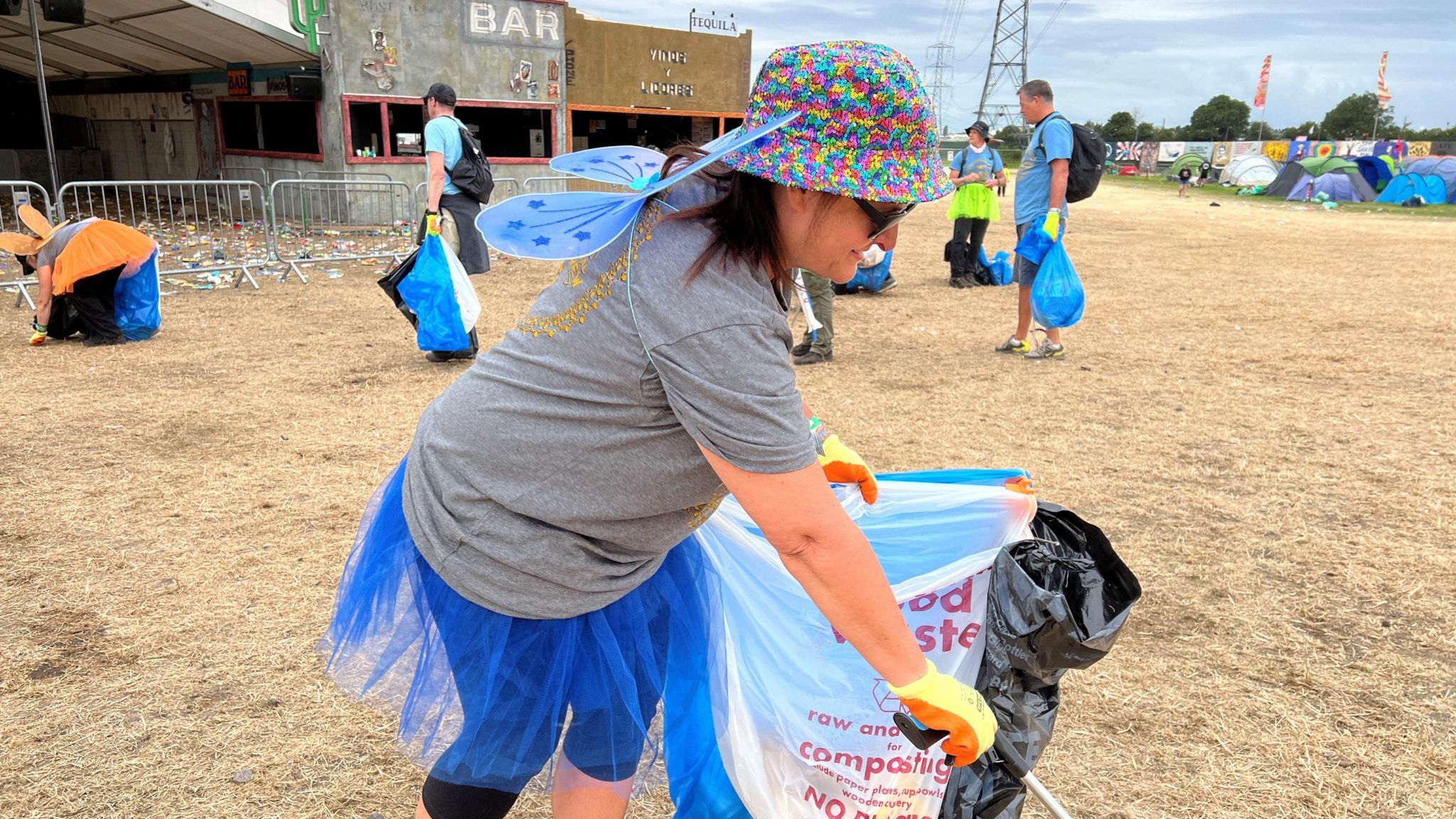 Women with fairy wings clearing rubbish with a bin bag in one hand