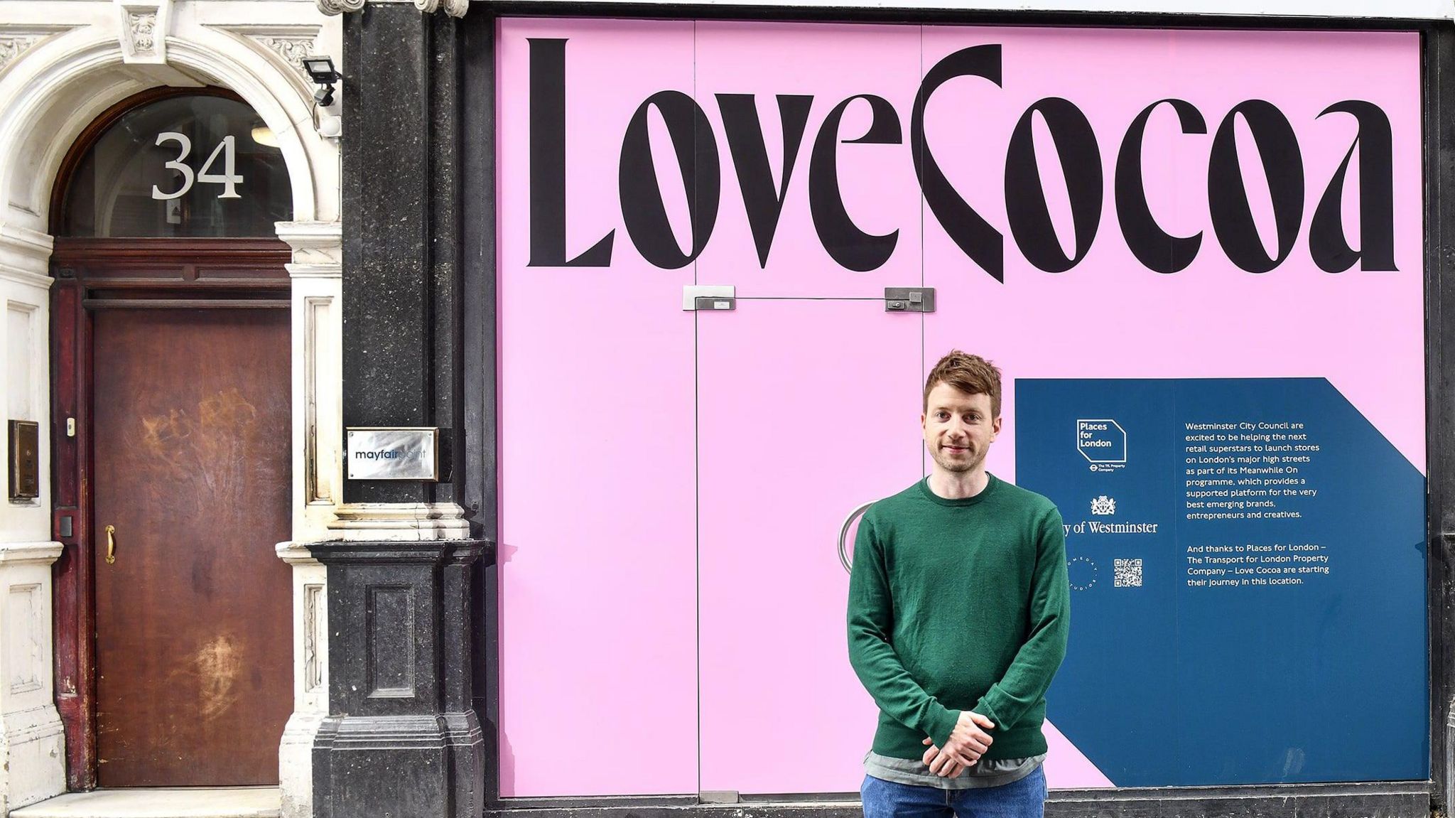 Man stands in front of pink shop sign that reads: Love Cocoa