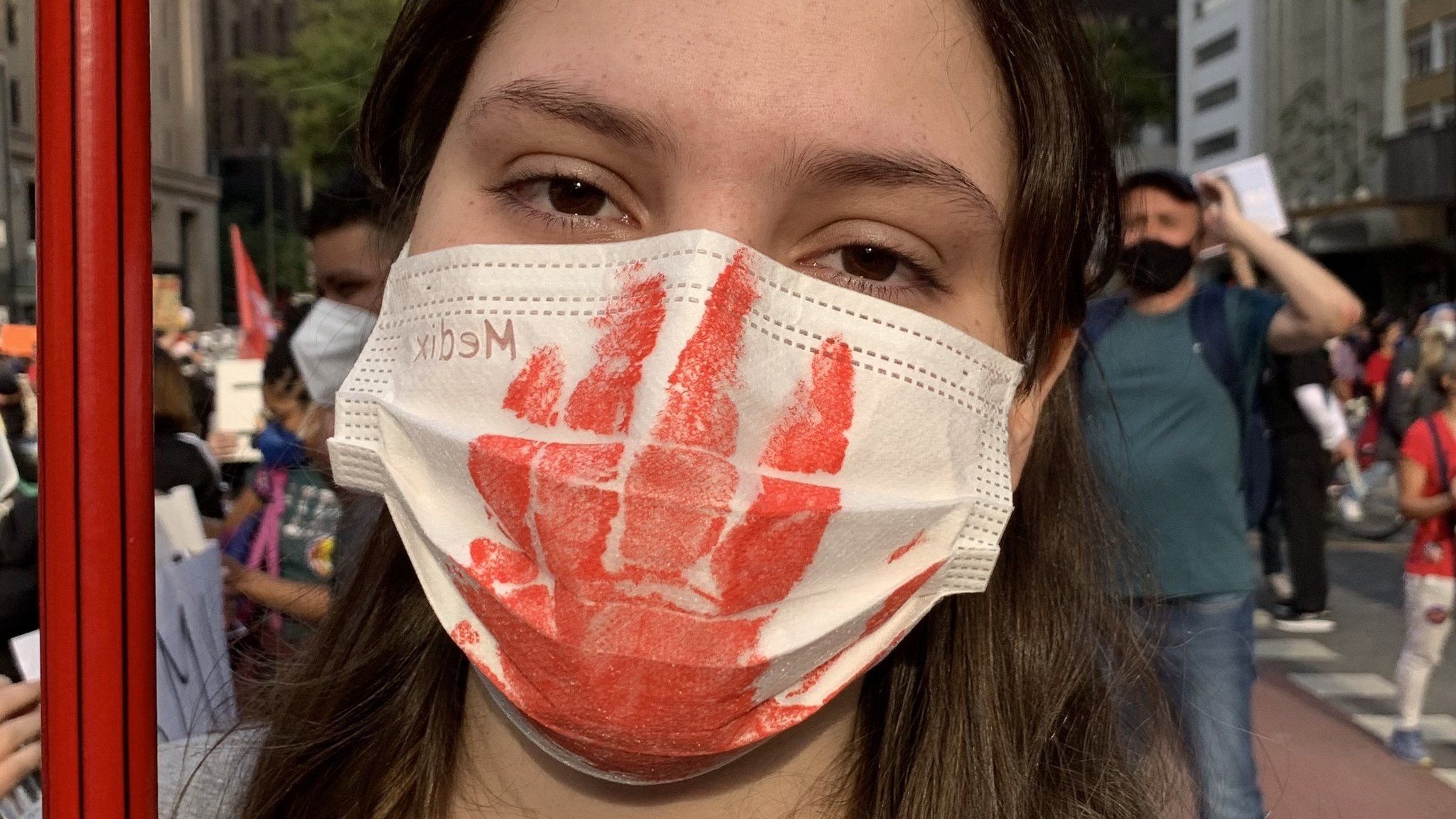 A woman wears a mask with a bloody hand print printed on it
