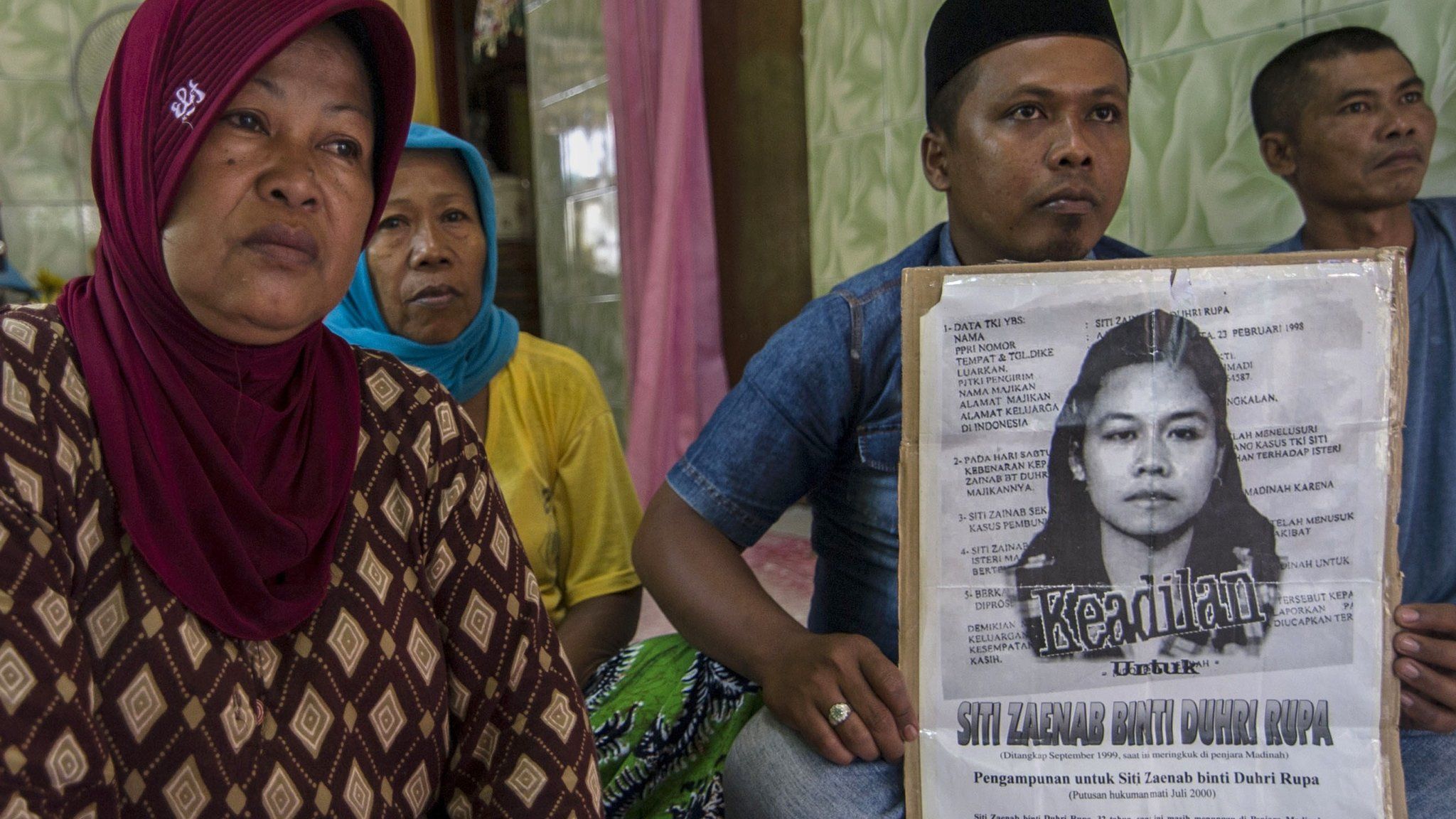 Family members of beheaded Indonesian maid Siti Zainab hold up a poster (R) bearing her portrait at their family home in Bangkalan in East Java province on 15 April 2015