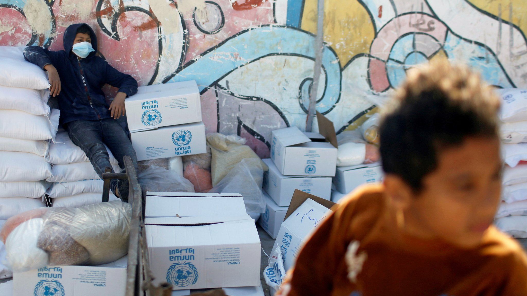 A Palestinian boy sits on a bag of flour at an aid distribution centre run by the United Nations Relief and Works Agency (Unrwa) in Gaza City (20 January 2021)