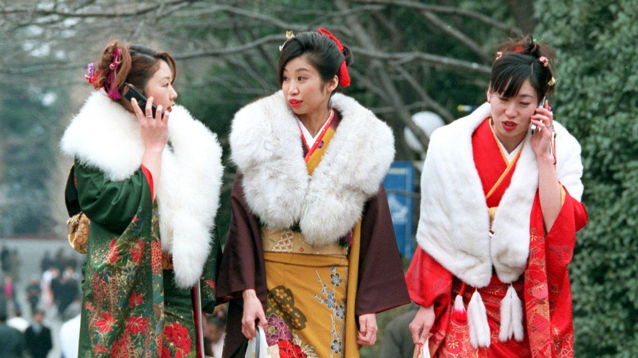 Three Japanese kimono-clad women make phone calls as they leave an annual coming-of-age ceremony