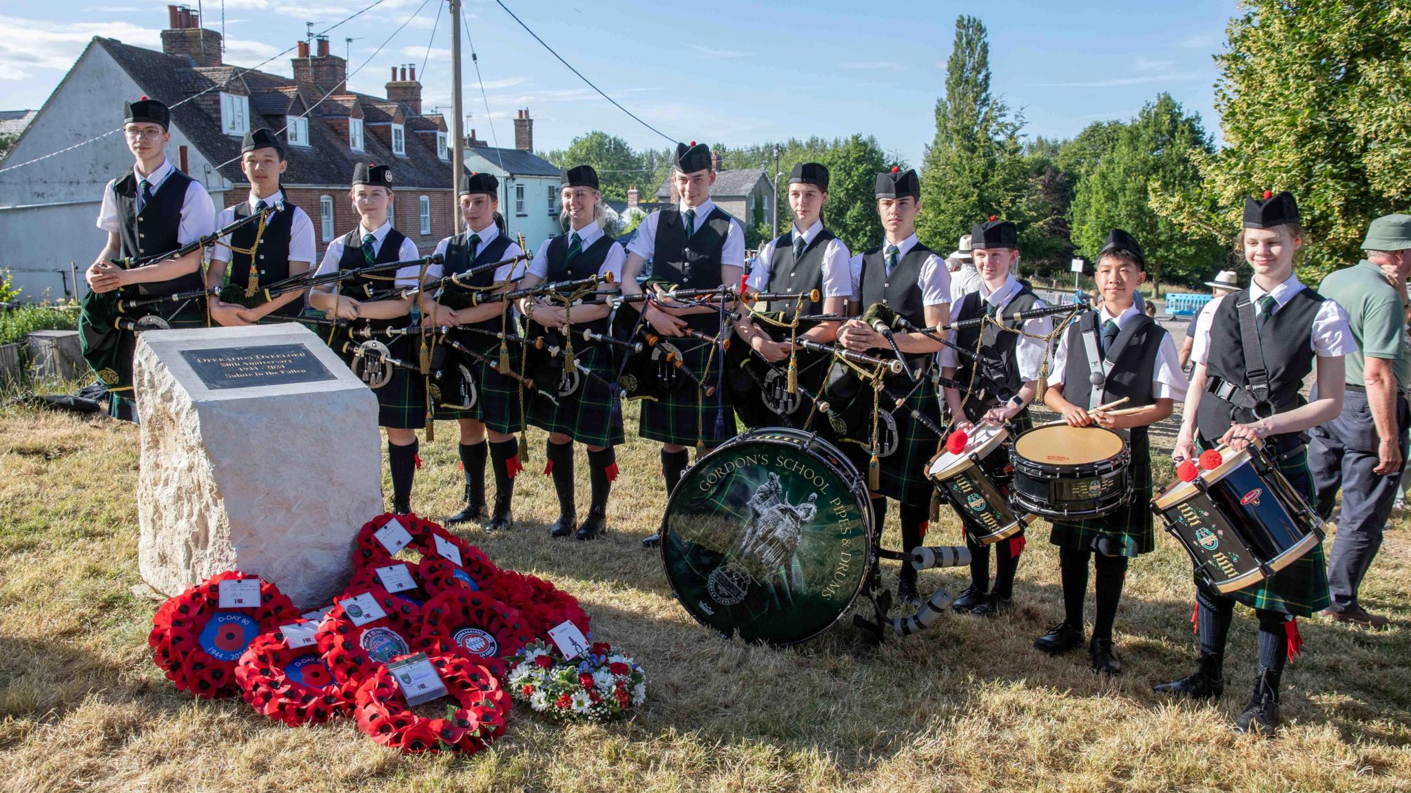 A commemorative stone, surrounded by poppy wreath and pipe and drums band