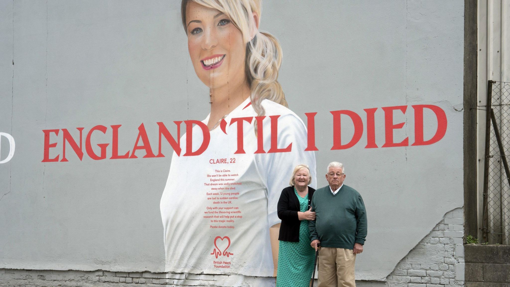 An older couple standing in front of the mural, which depicts a young woman with the slogan 'England til I died'