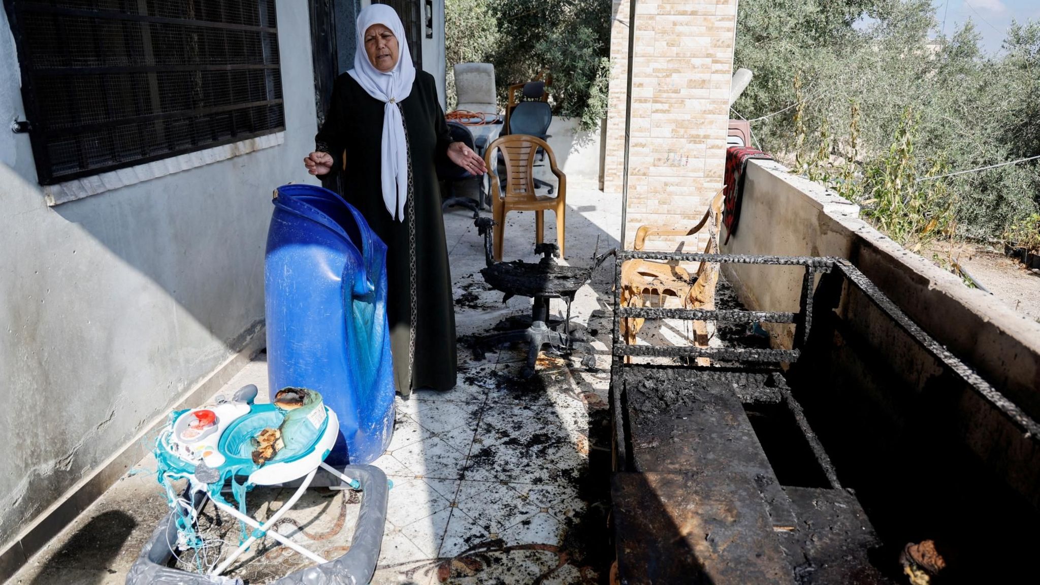 A Palestinian woman gestures towards furniture and a baby walker burned in an attack by Israeli settlers in the village of Jit, in the occupied West Bank (16 August 2024)