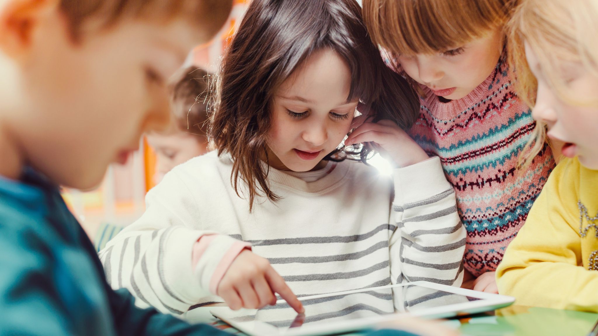 A group of young children gather round a ipad