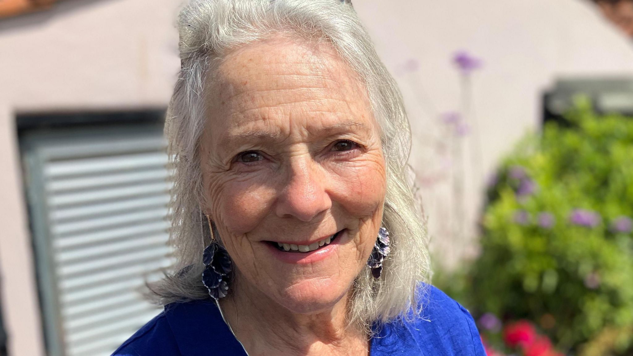 Candida Leaver wearing blue top and smiling while standing in a garden.