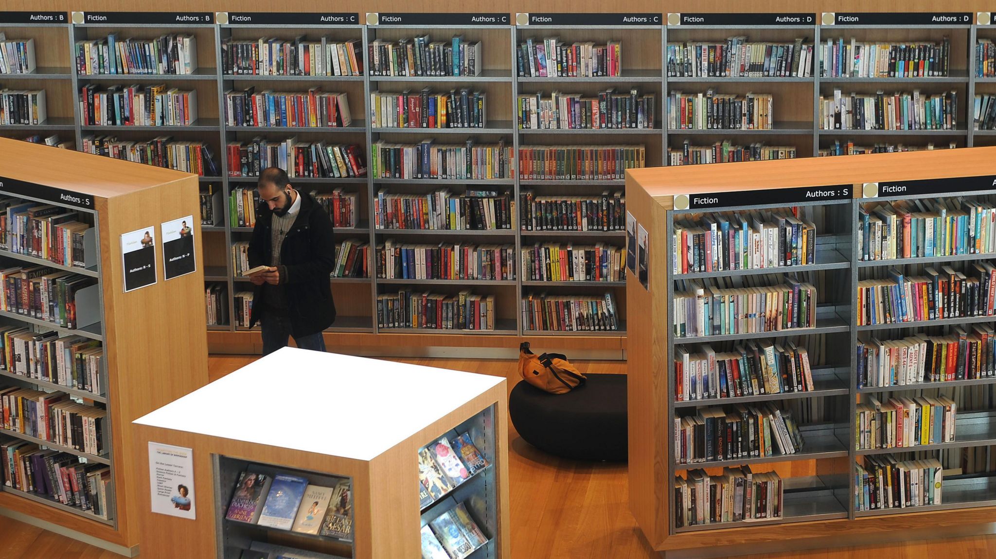 Man looks at book surrounded by bookshelves in library