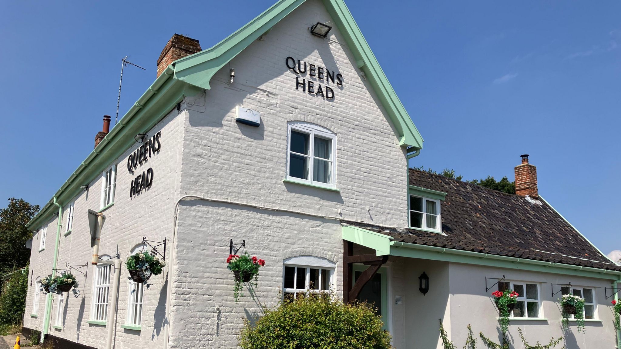 Painted white brick facade of the Queens Head pub with flowers in baskets hanging from the walls