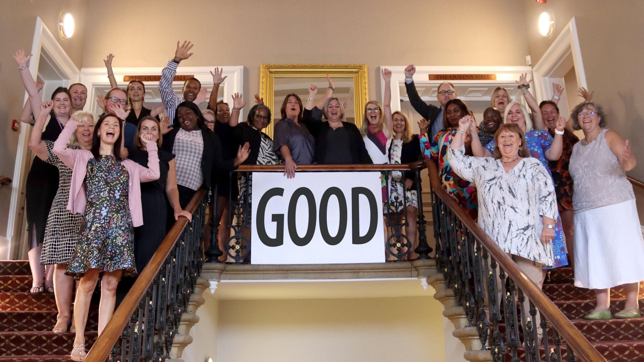 Staff standing on the stairs cheering around a "good" sign