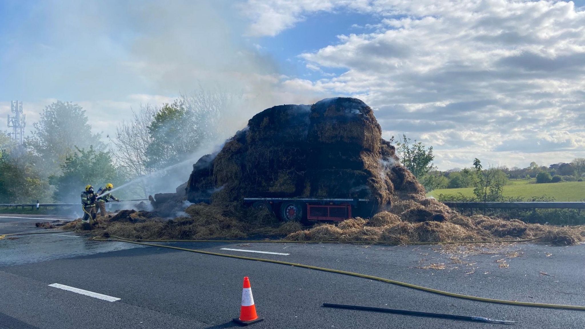 Fire crews blast a lorry carrying hay, which is on fire, with water hoses