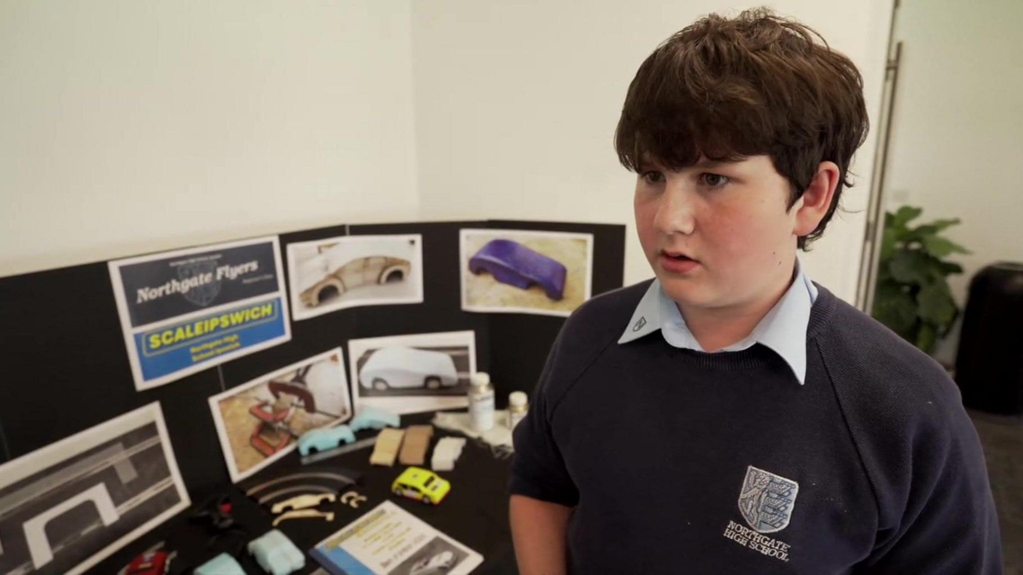 A school pupil looking to the left. Behind him are designs on a board for a toy car