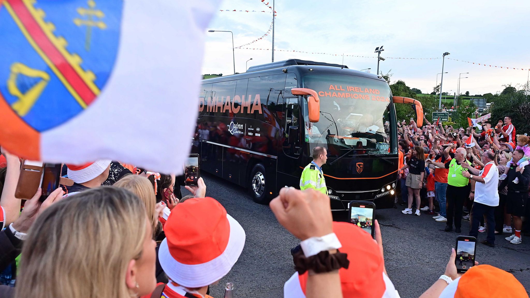 Fans surrounding a coach. They're waving flags and cheering.