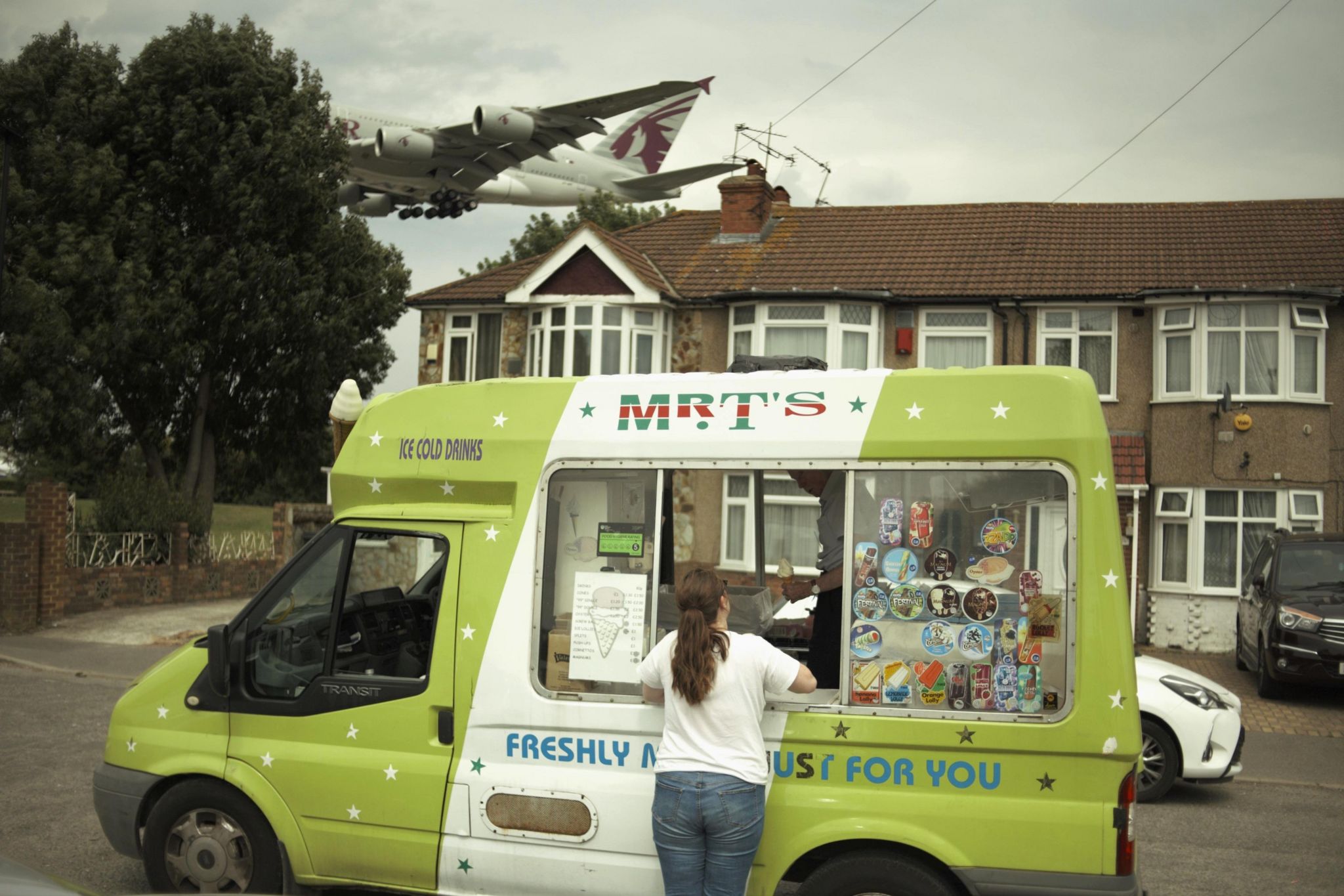 Woman buy ice cream from ice cream van with plane in background