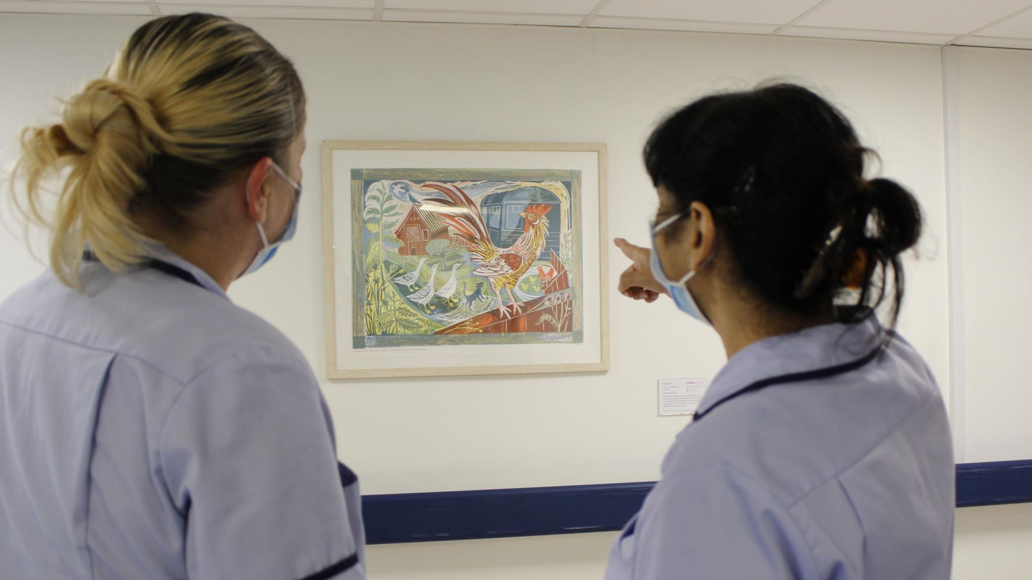 Two nurses looking at a painting on a hospital wall