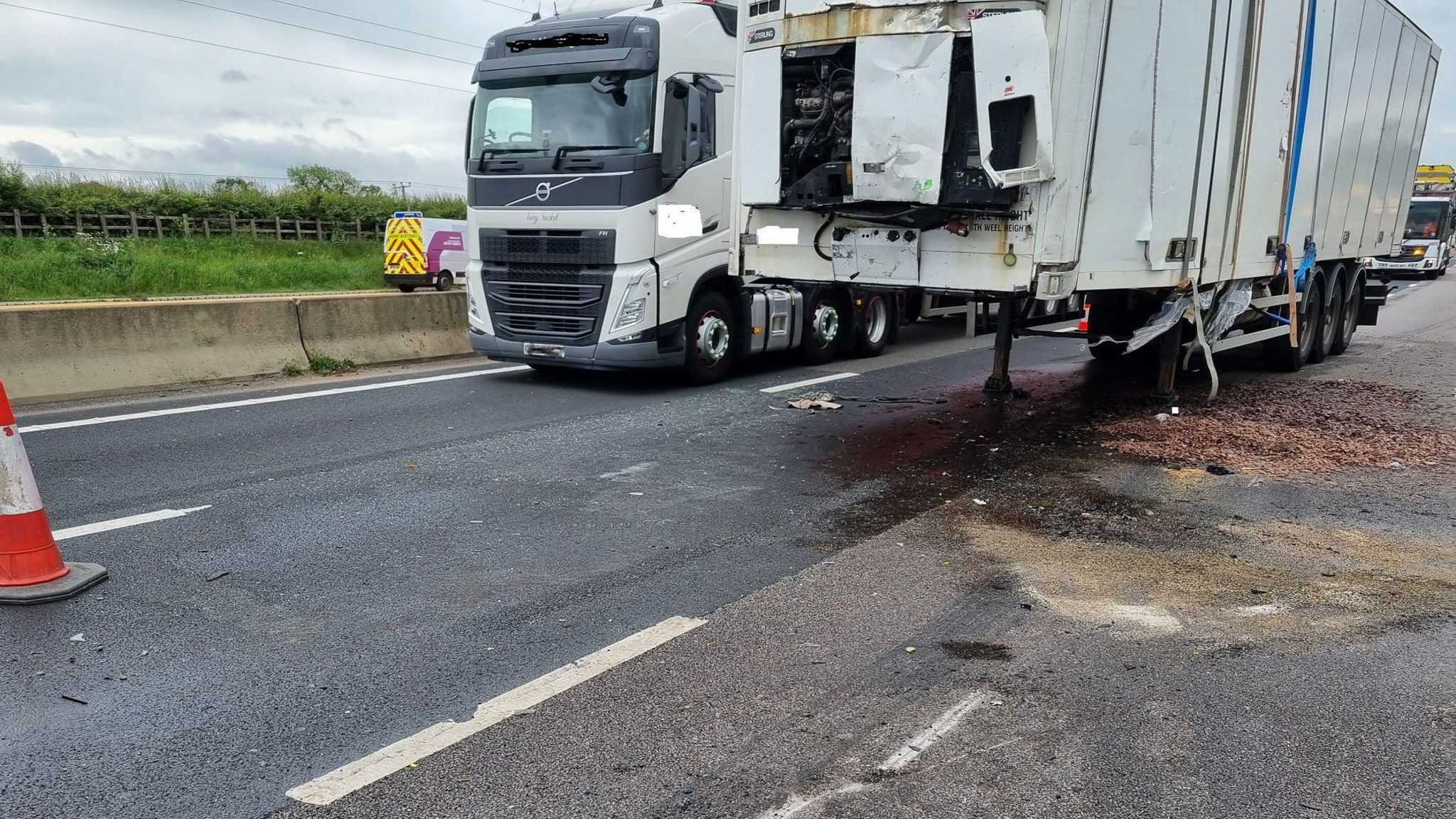The large white lorry is seen from the front and there is debris on the tarmac