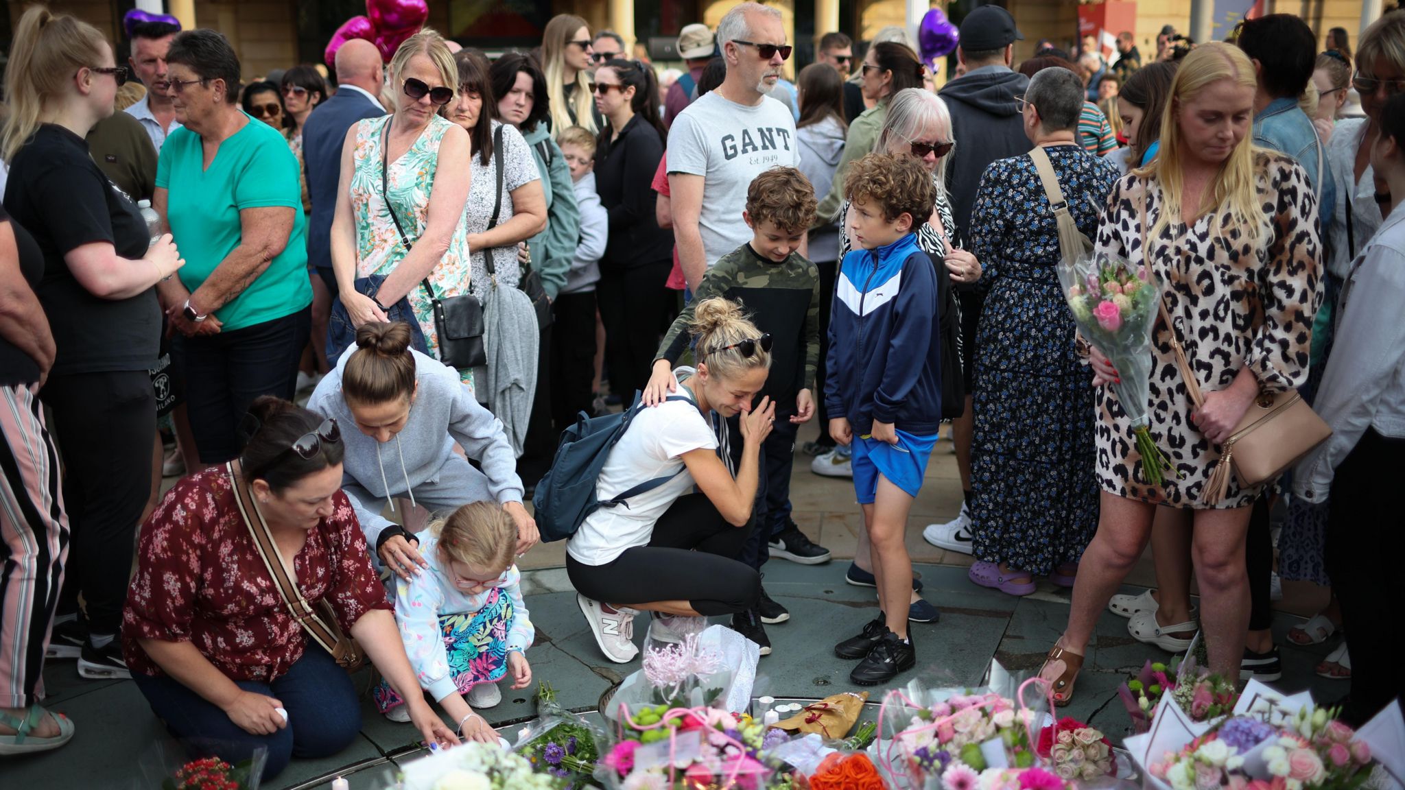 A crowd of people, ranging from young children to grey-haired adults, light candles and leave floral tributes to the victims of the Southport attack, some bowing their heads in sadness, others holding each other for comfort