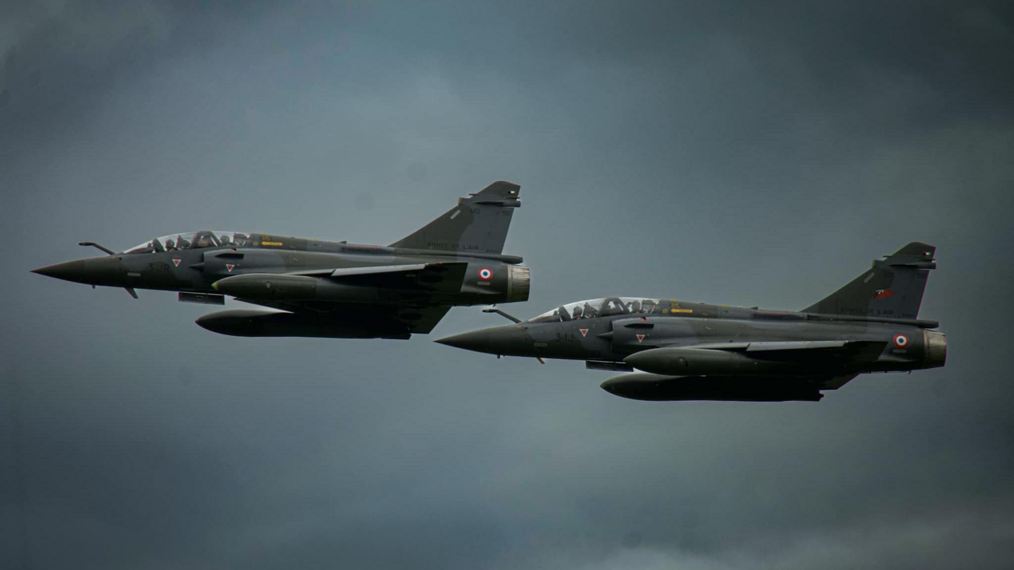 Two aircraft fly side by side in the grey sky