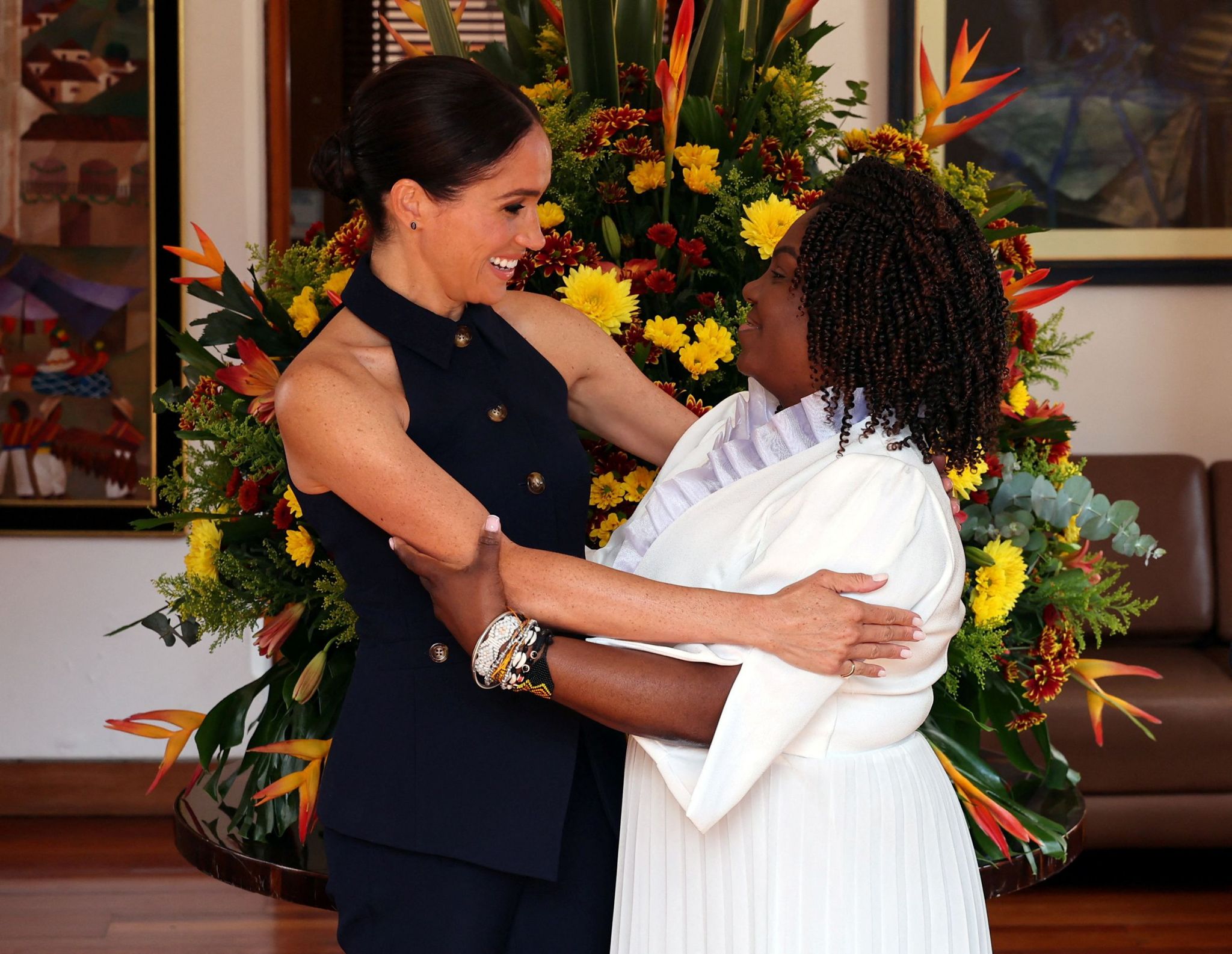 A smiling Meghan, Duchess of Sussex, embraces Colombia's Vice President Francia Marquez in front of a large bunch of flowers. 