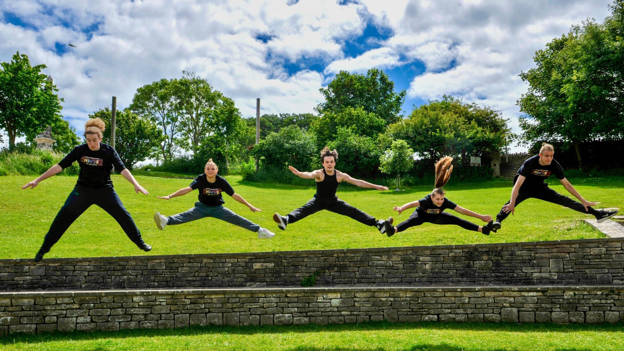TUESDAY - Five young people wearing black tshirts jump out from being a stone wall in Swanage