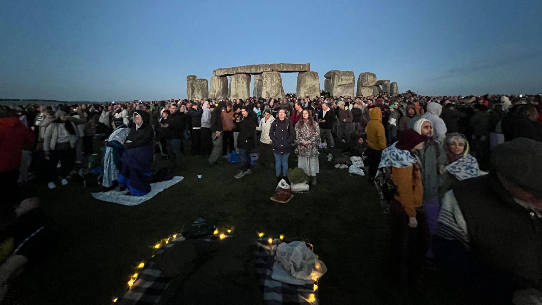 A darkened sky and people waiting for the sunrise in front of Stonehenge