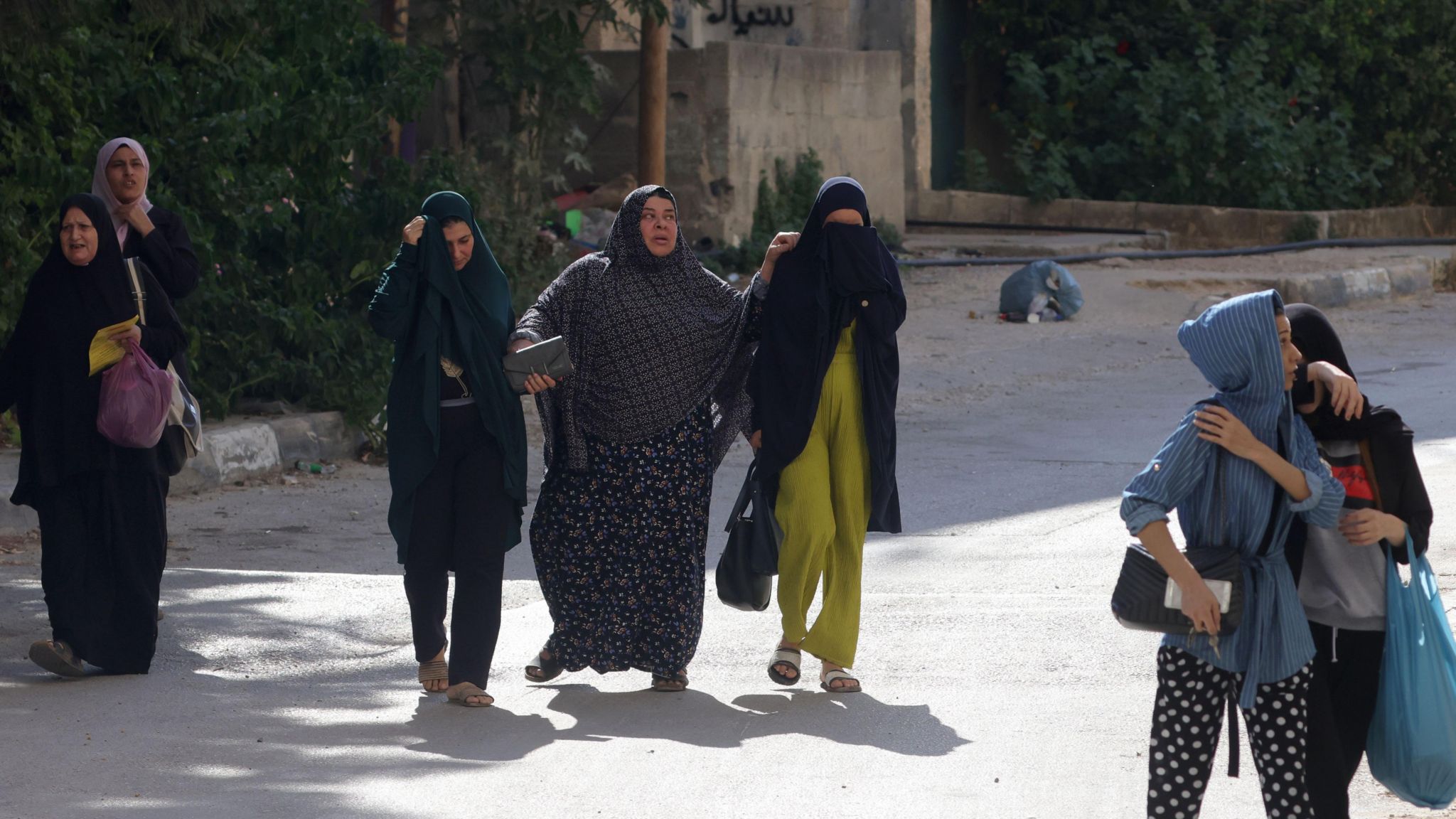 Palestinians, among them women and children, walk past Israeli troops as they leave Jenin refugee camp, 31 August 2024