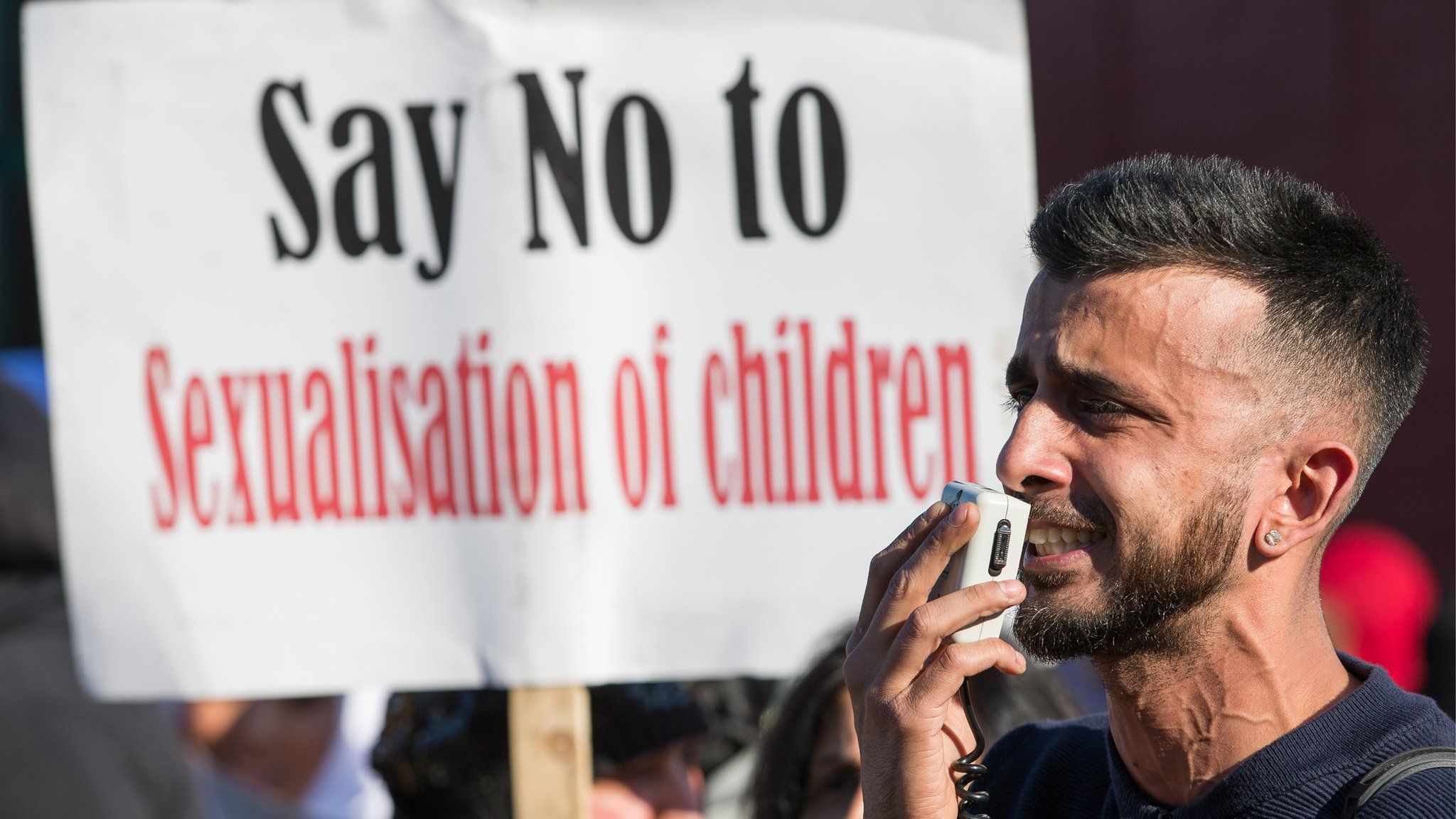 Police and parents at a protest outside a school. A placard reads "Say no to sexualisation of children"