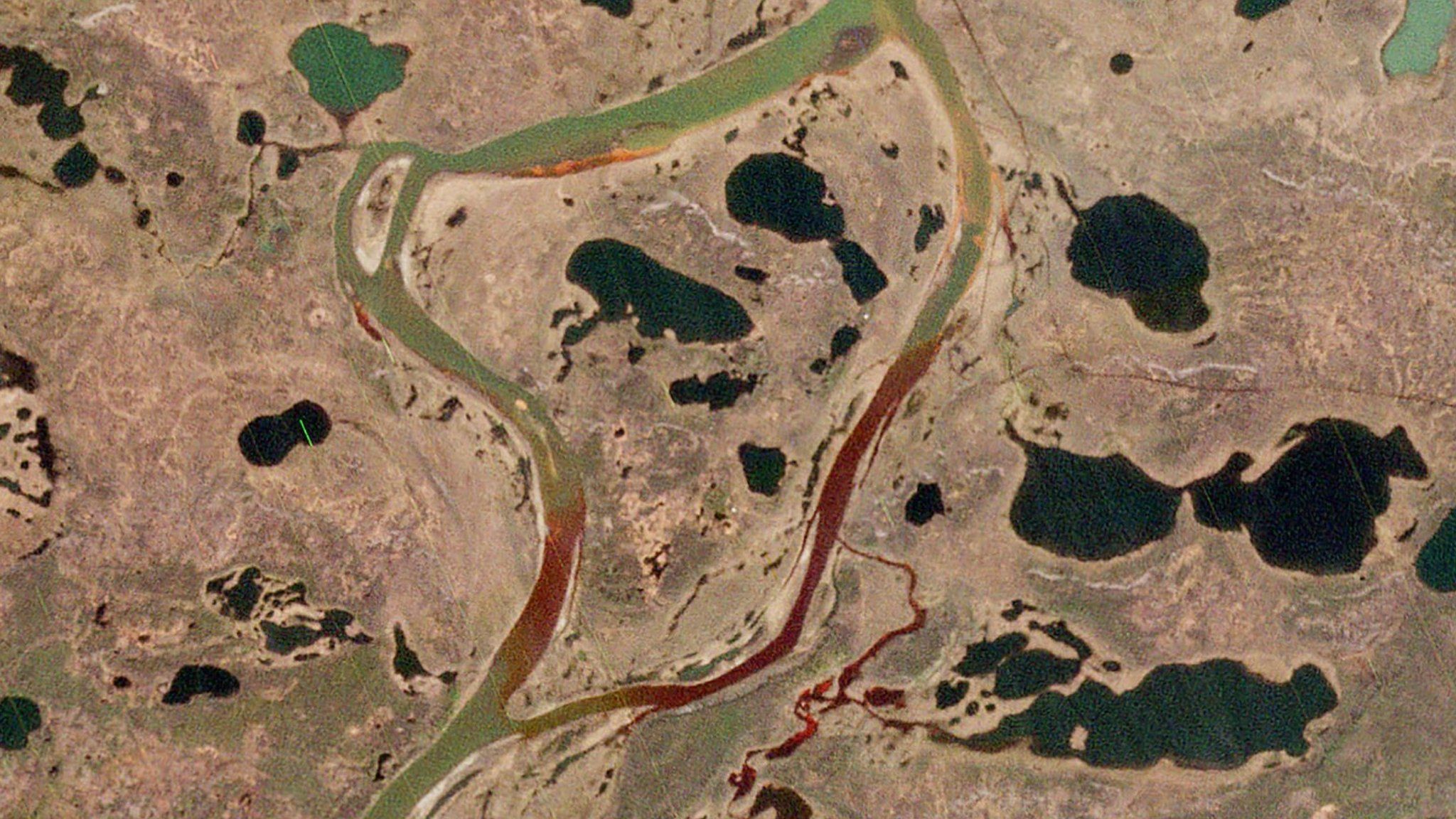 A river is coloured red by an oil slick in the Arctic