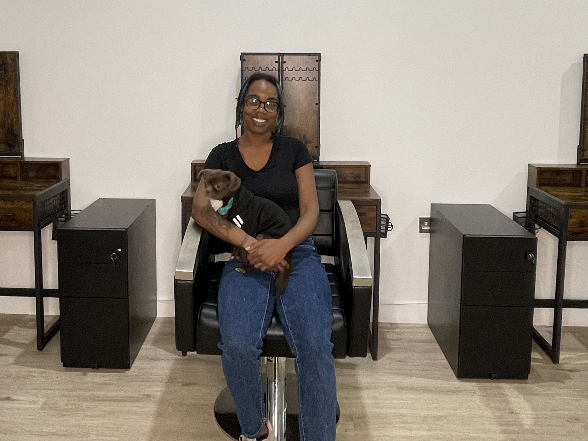 A woman sat on a salon chair with a dog on her lap