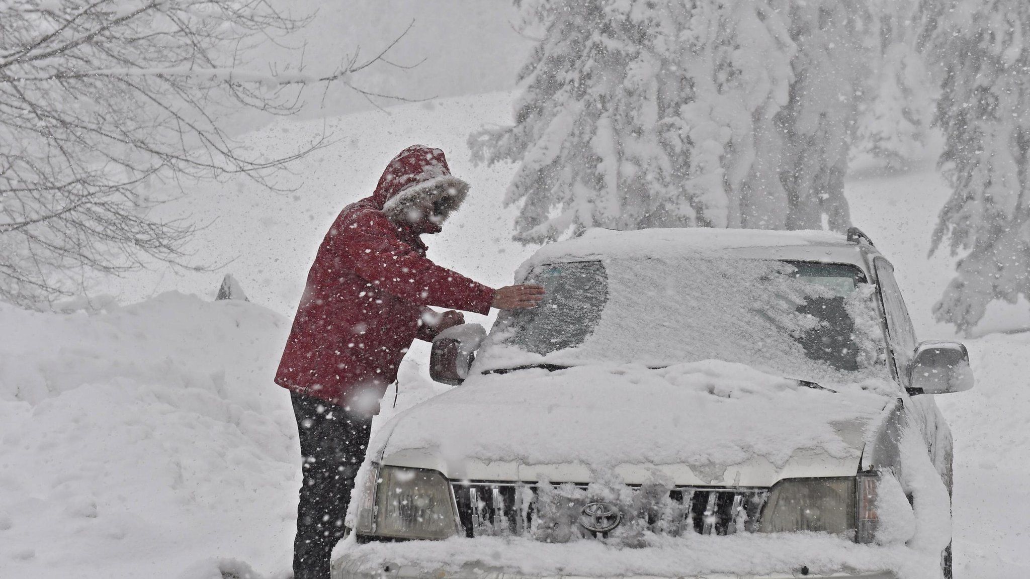 A person clears snow from a vehicle after a heavy snowfall in Casaglia, Mugello, Florence"s province, Italy