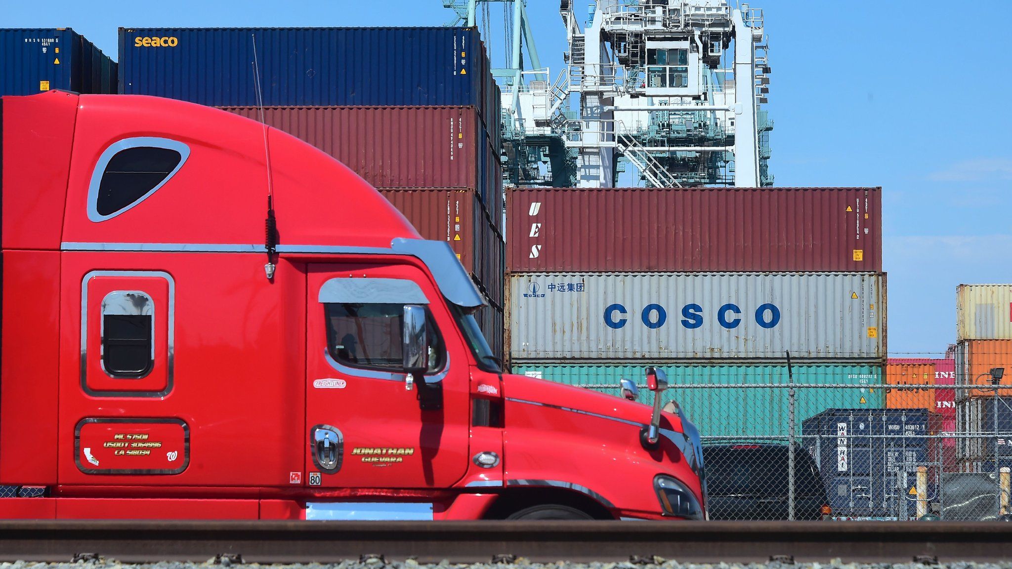 In this file photo taken on July 6, 2018 a container delivery truck passes containers stacked at the Port of Long Beach in Long Beach, California including one from COSCO, the Chinese state-owned shipping and logistics company.