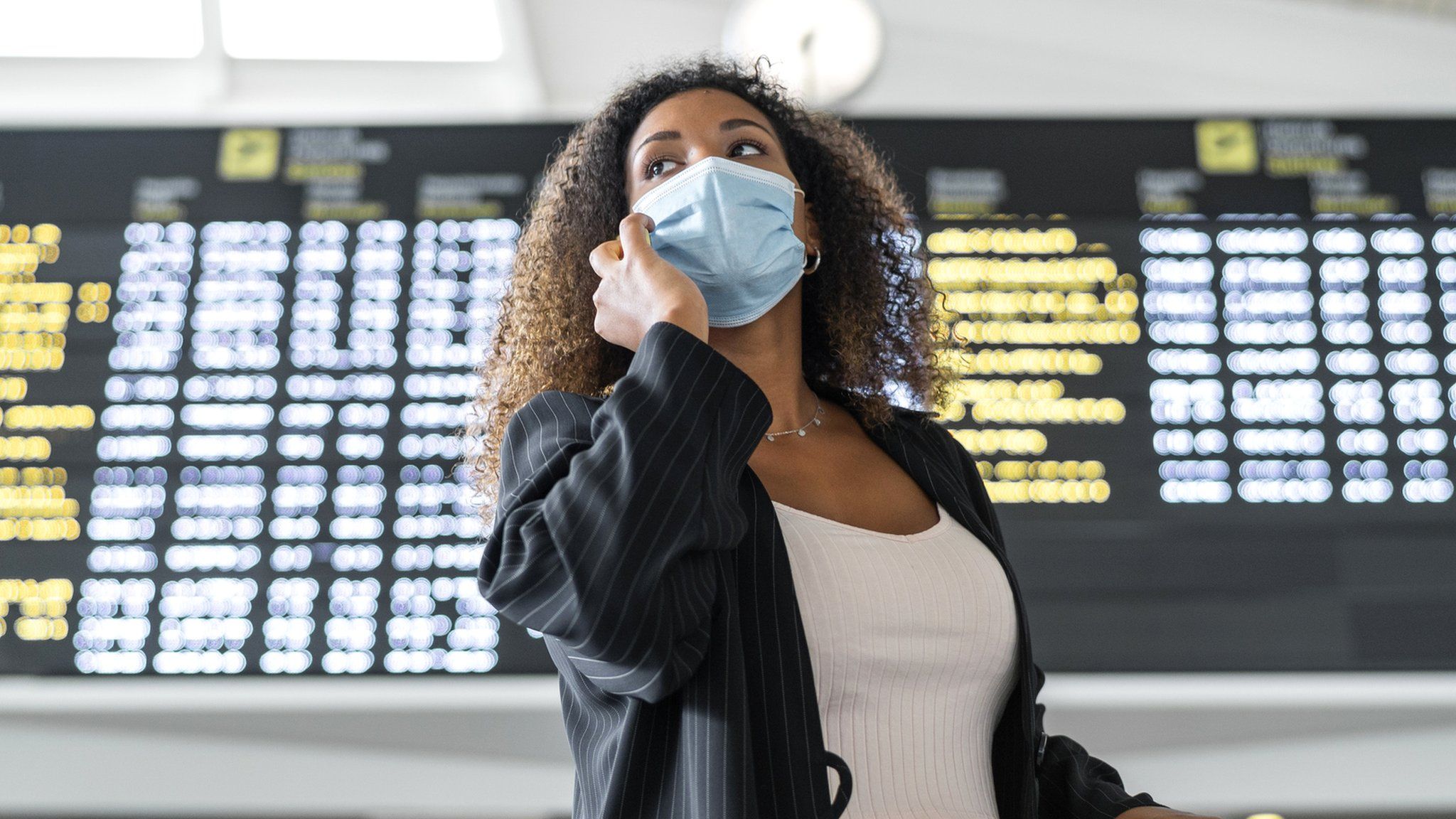 A woman in a mask in front of a departure sign